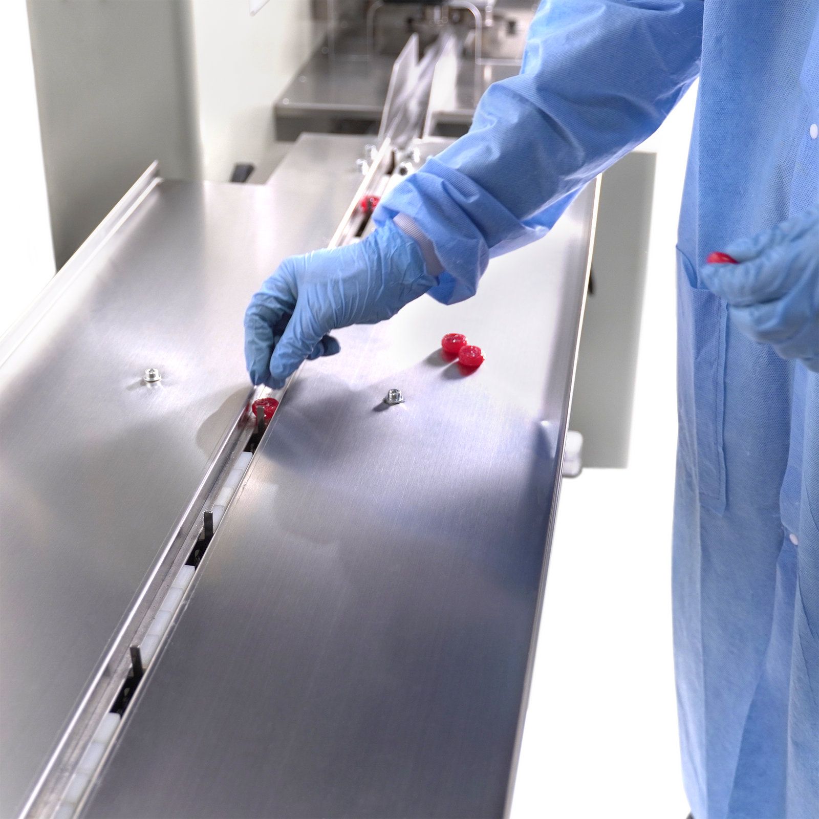 Worker inserting small candies into the conveyor of the automatic flow wrapper with inverted film feeder for pillow bag forming