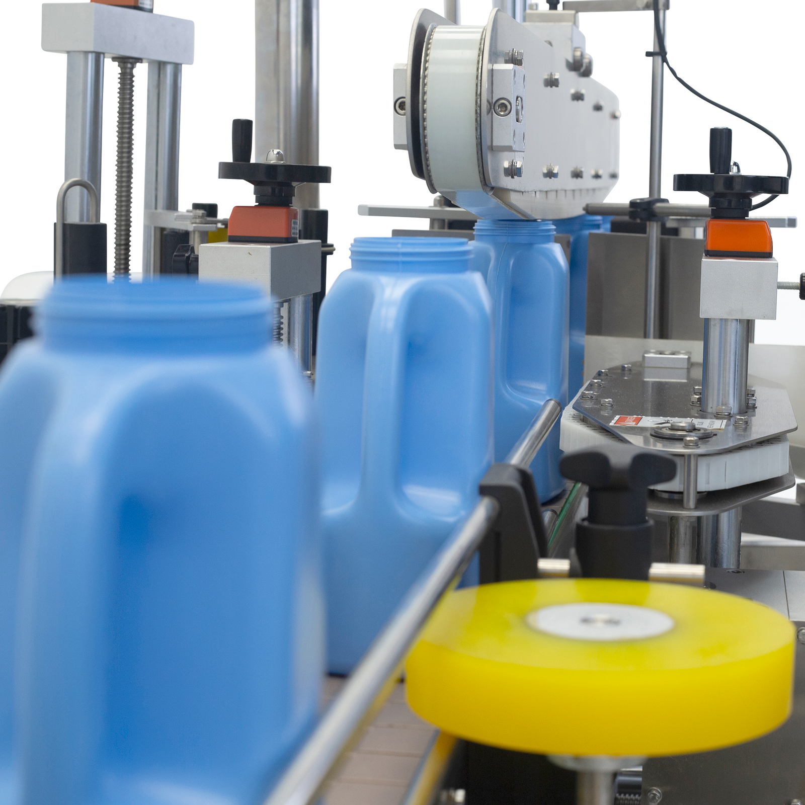 closeup showing the JORES TECHNOLOGIES® automatic-label applicator under production with 5 blue oval plastic containers on the conveyor integrated to the machine