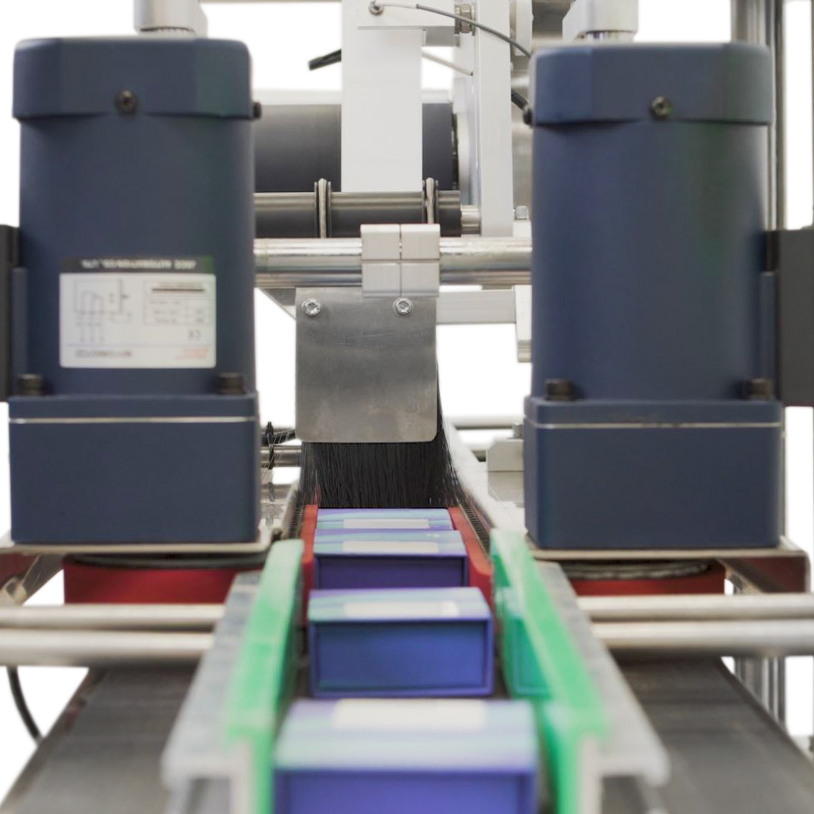 The automatic labeler under production attaching labels on top of  blue small flat boxes placed on the conveyor of the JORES TECHNOLOGIES® automatic label applicator