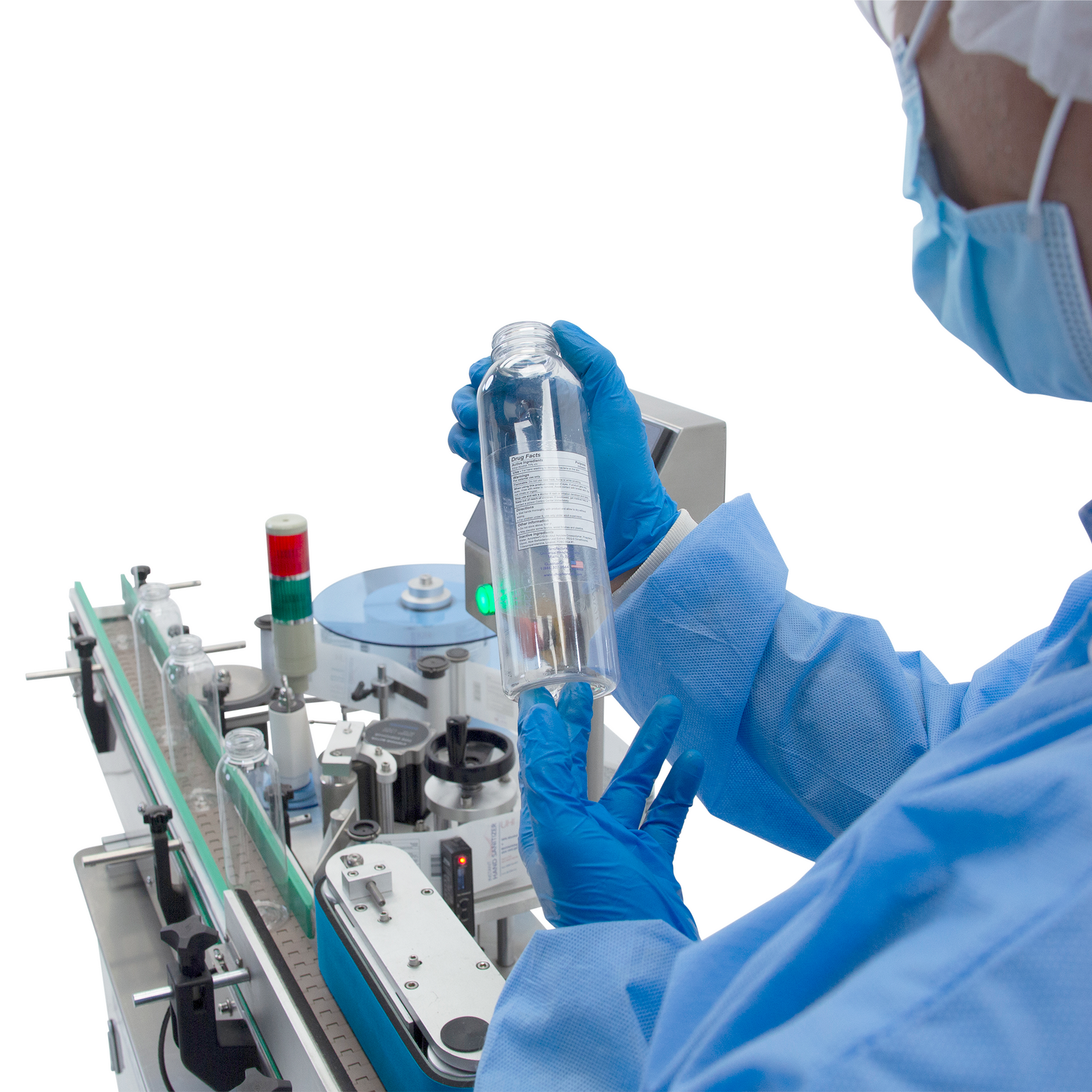 operator wearing blue protective gown looking at clear bottle with white label with of automatic label applicator in the back ground