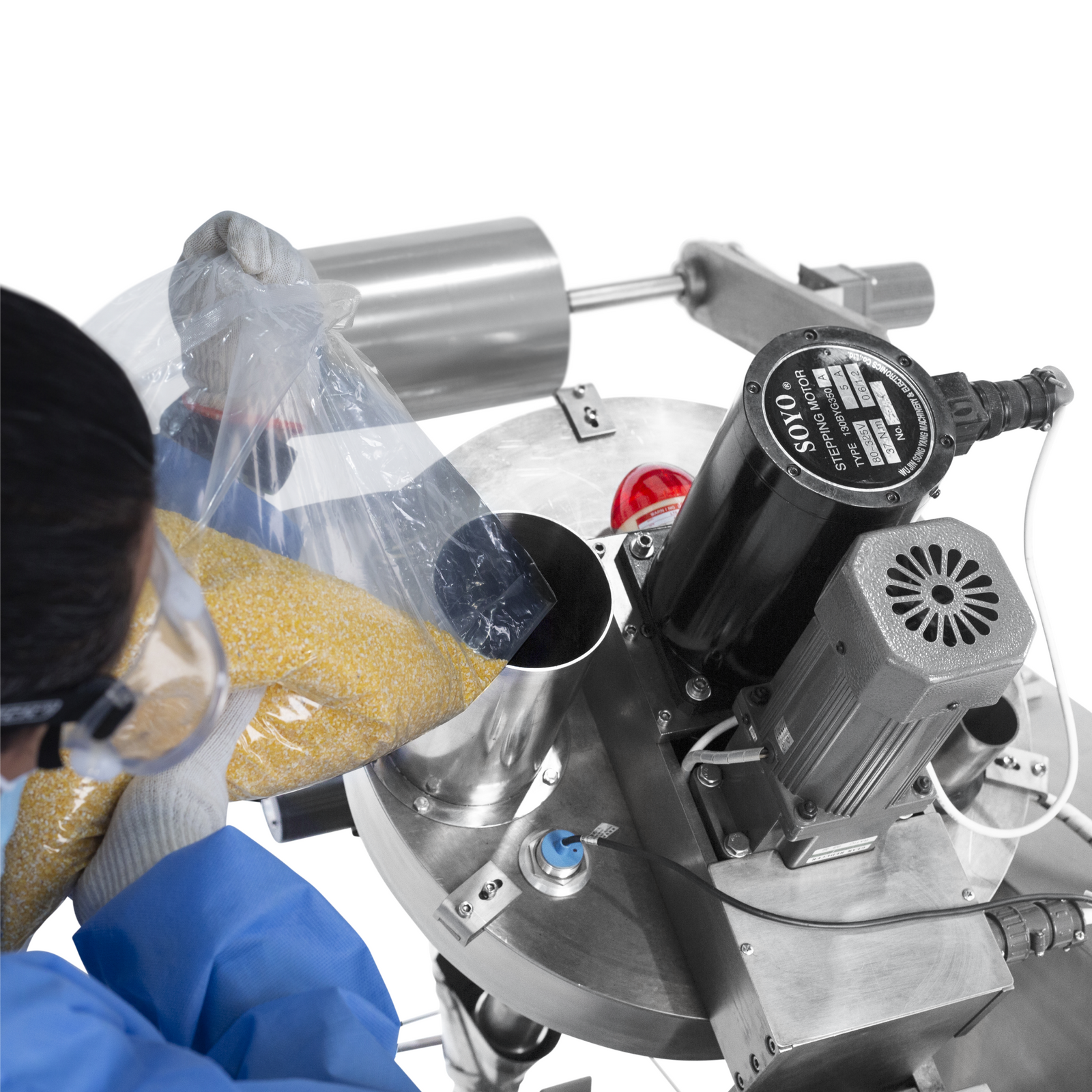 Top view of an operator wearing a blue disposable PPE gown, emptying a granulated powder into the hopper ofa vertical form, fill & seal (VFFS) system 