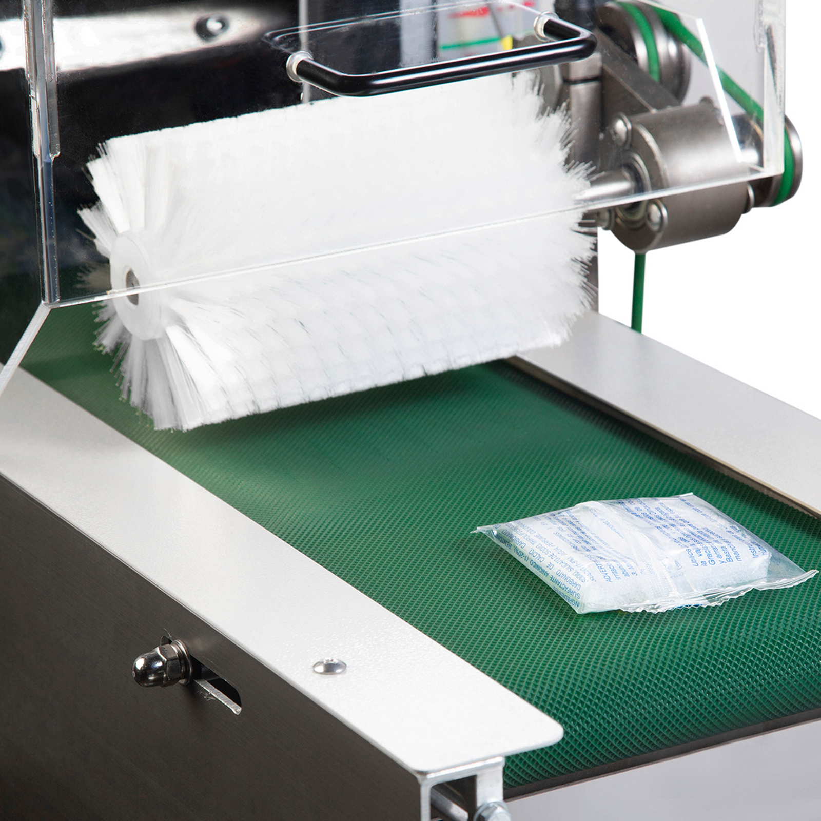 Pillow package with a product inside, on a textured green exit takeaway conveyor after being sealed by an inverted HFFS automatic flow wrapping machine