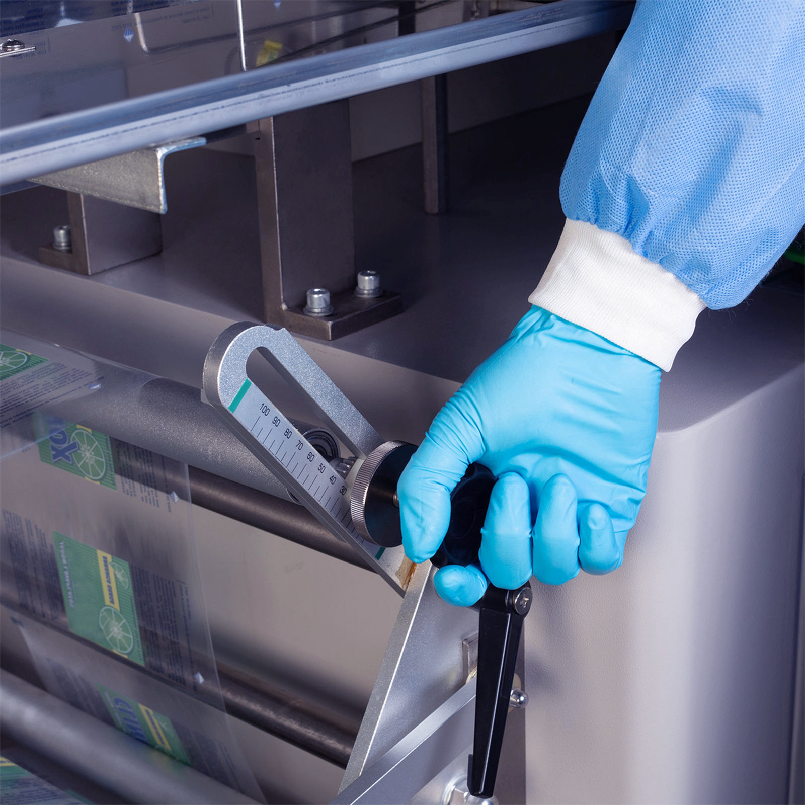 Operator wearing blue PPE disposable gloves and a gown can be seen adjusting the machine's packaging film roll dispenser