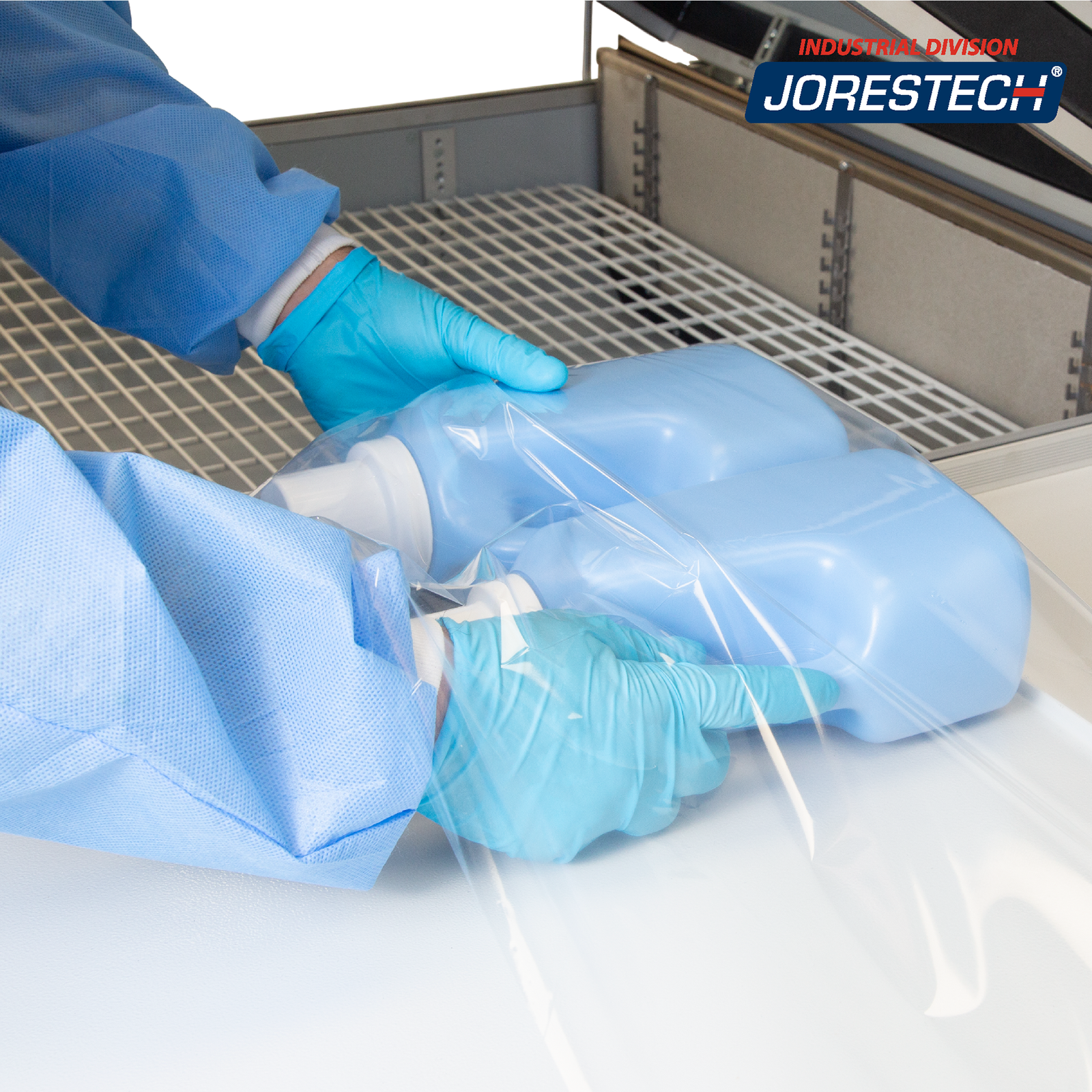 Close up of the shrink chamber of a JORES TECHNOLOGIES® shrink wrapping system showing the hands of a person inserting 2 containers in the center folded film before placing the bundle to be shrunk inside the heat shrink chamber.