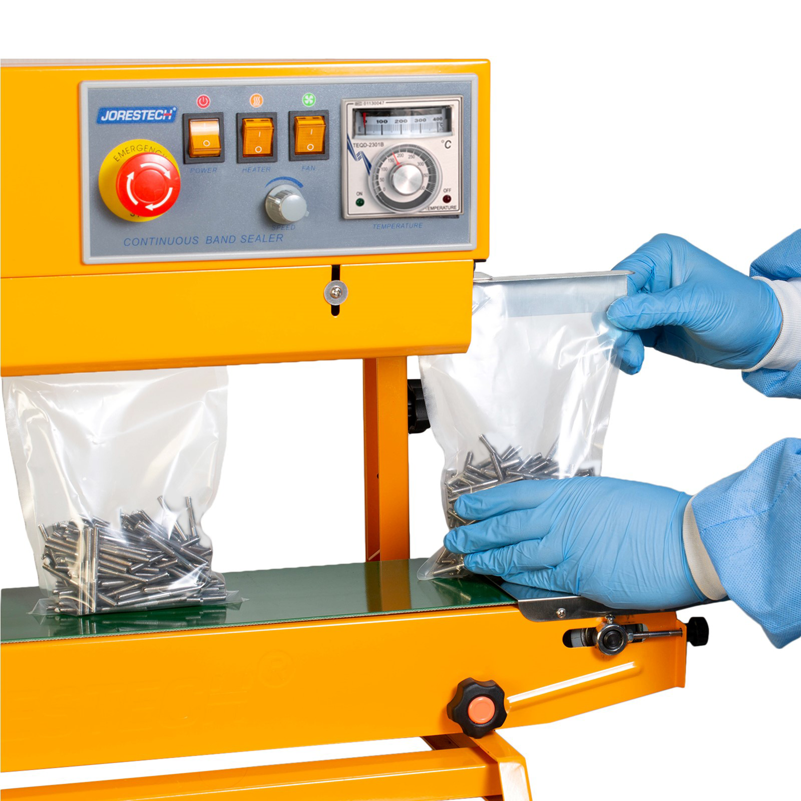 Worker wearing PPE inserting plastic bags filled with nails into the yellow JORES TECHNOLOGIES® continuous heat bag sealer. The bag sealer is positioned for vertical applications