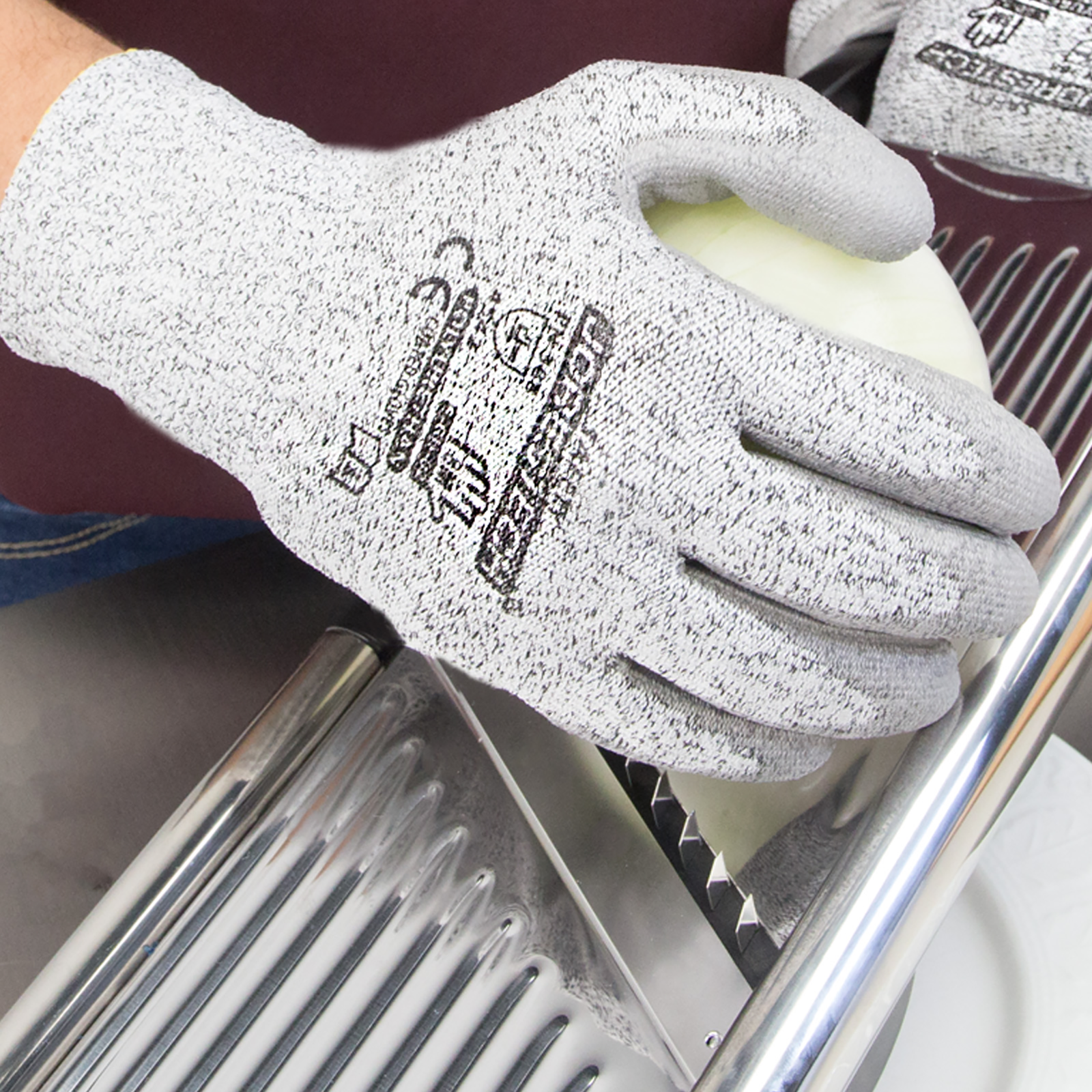 Person wearing the cut resistant JORESTECH gray safety work gloves with polyurethane dipped palm while cutting an onion with a silver metal blades slicer