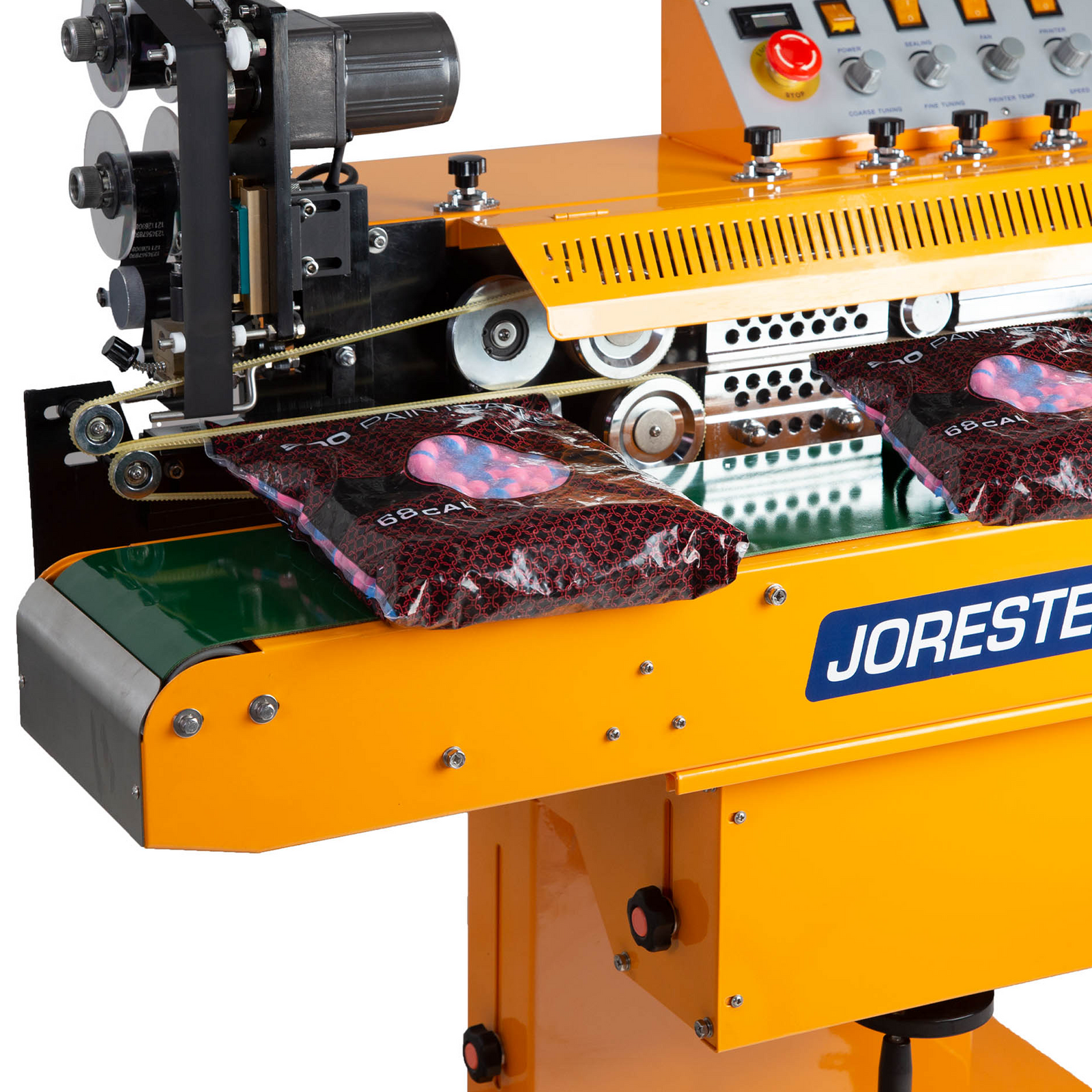 close up of the yellow JORESTECH horizontal continuous band sealer with wheels  sealing and hot stamp coding plastic bags filled with blue and pink balls. Also shows the hot stamp coder of the continuous band sealer wit a roll of black hot stamp ink roll installed