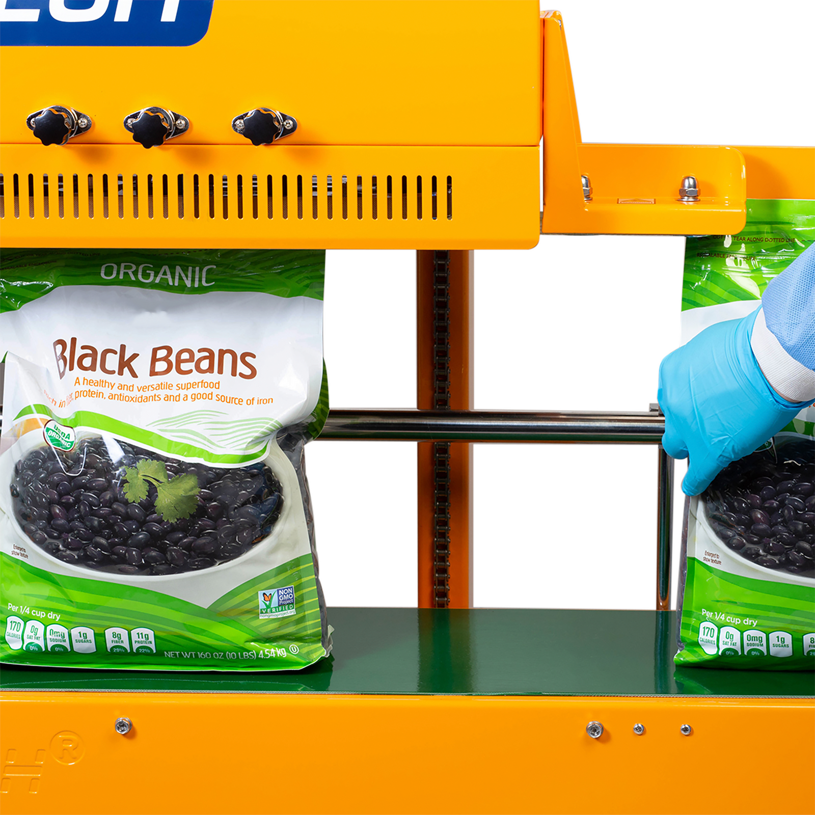 Operator wearing disposable blue clothing sealing and coding 10 pound large plastic bags filled with black beans with a vertical JORES TECHNOLOGIES® continuous band sealer for sealing vertically 