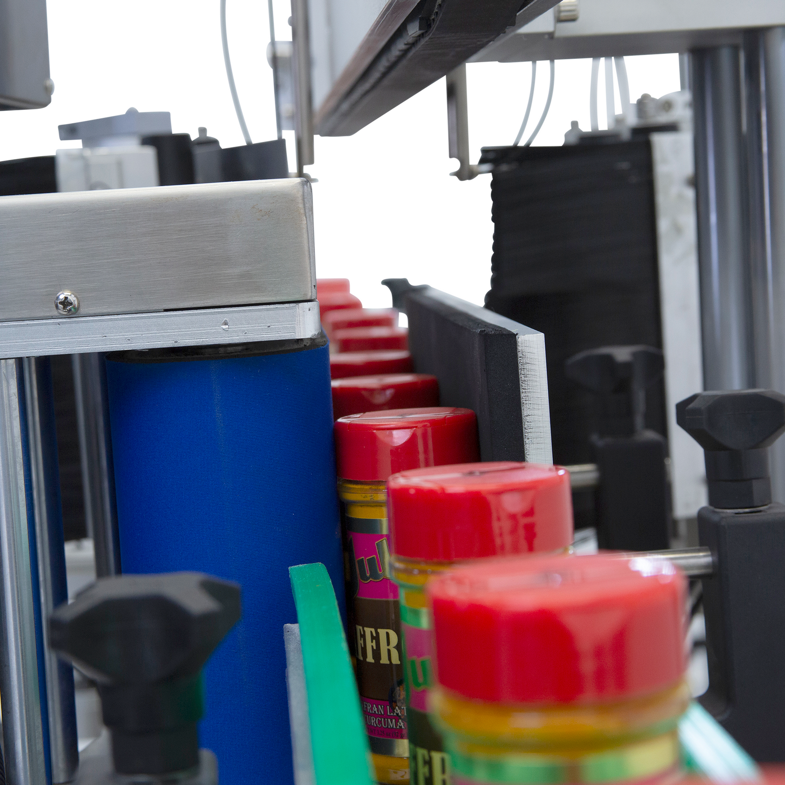 multiple seasoning round plastic containers with red caps going through the JORES TECHNOLOGIES® dual automatic label applicator 