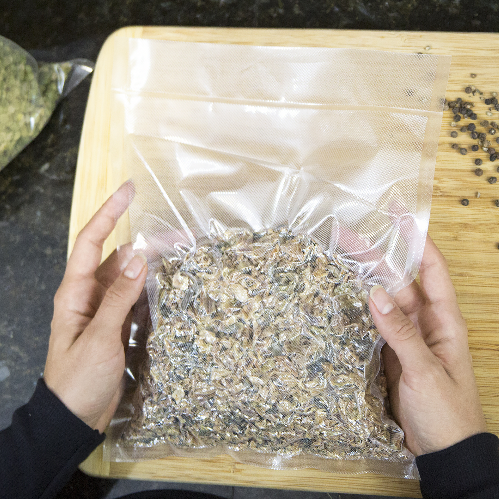 Person manipulating a vacuumed sealed embossed JORESTECH bag with tea or spiced inside in a kitchen setting using a brown cutting board