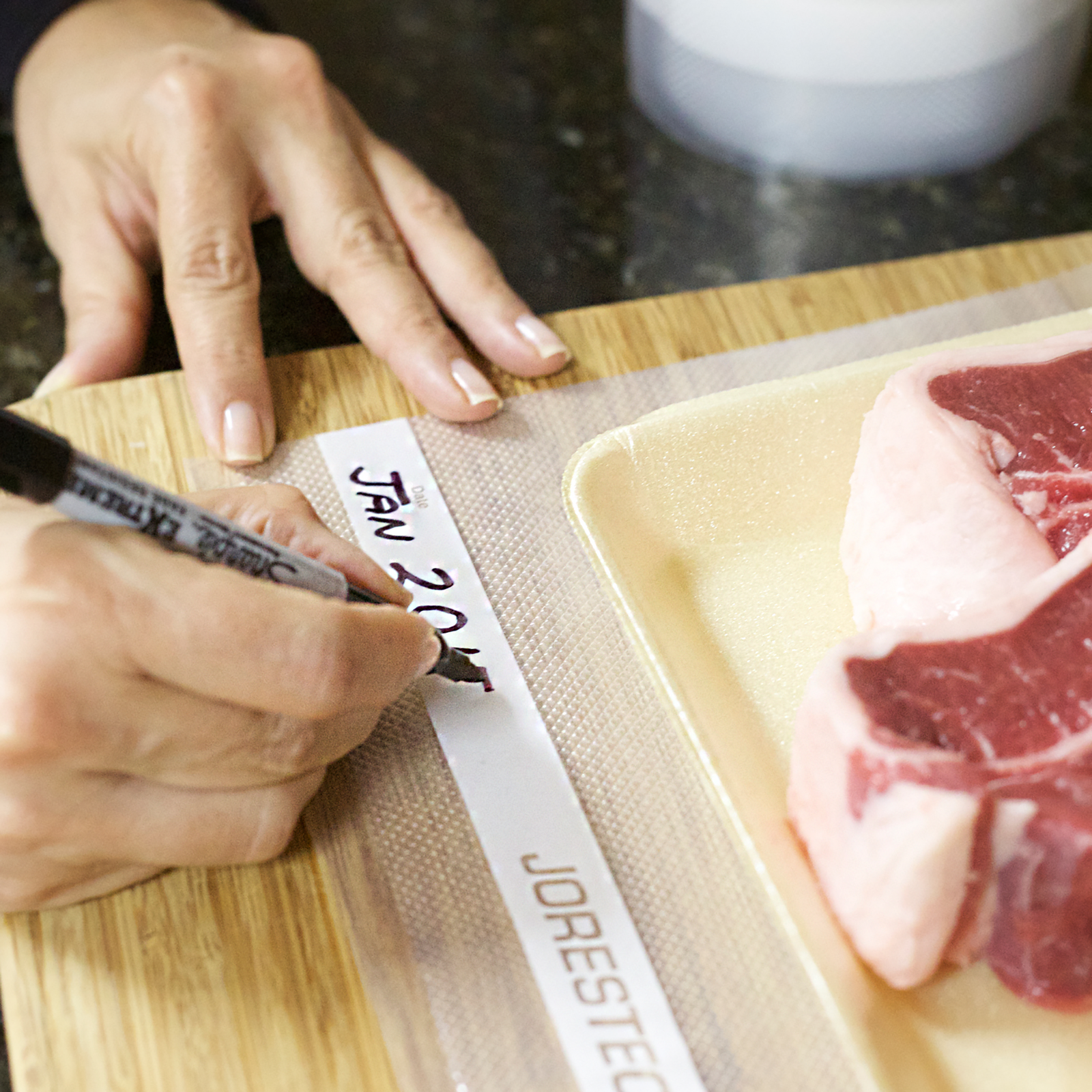 A person writing a date on the embossed JORESTECH vacuum sealer pouch filled with stakes that will go into a freezer. 