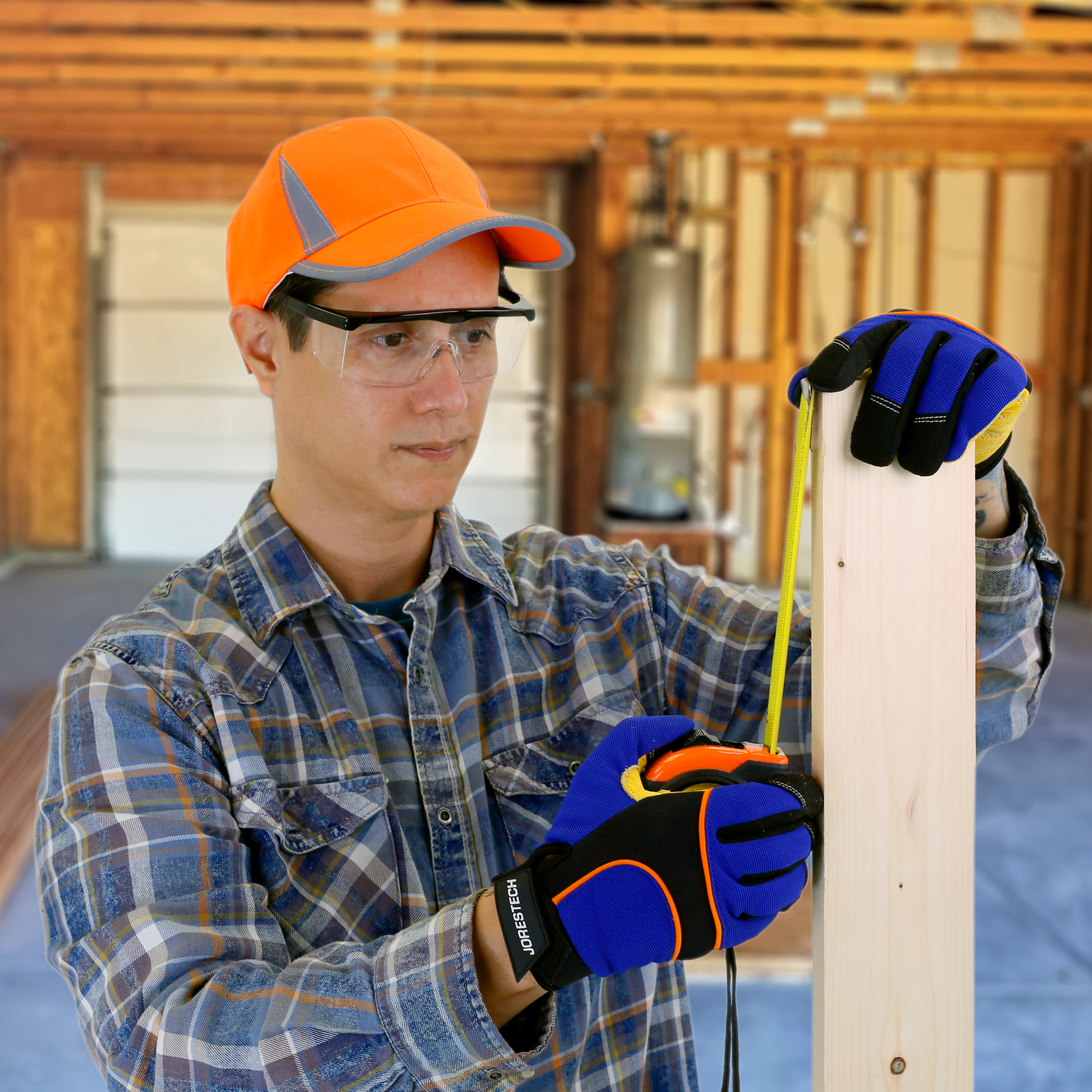 Man in a garage wearing safety gloves and the framed rectangular safety glasses with side shields for hi impact eye protection measuring a piece of wood uses in a DYI project 