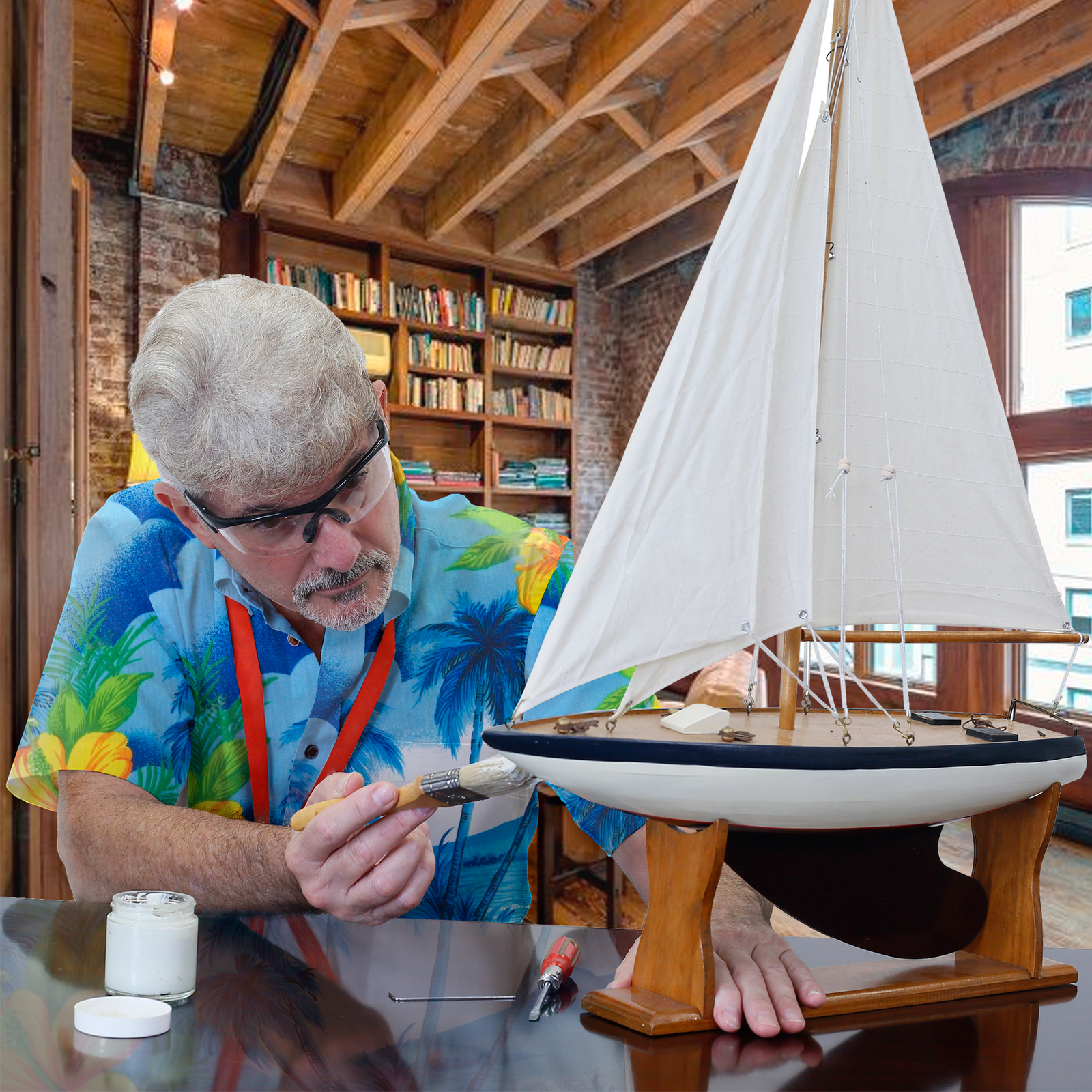 Man wearing the black framed JORESTECH ANSI compliant safety clear glasses with side shields for high impact protection while painting white a small decorative wood sail boat in his DIY studio.