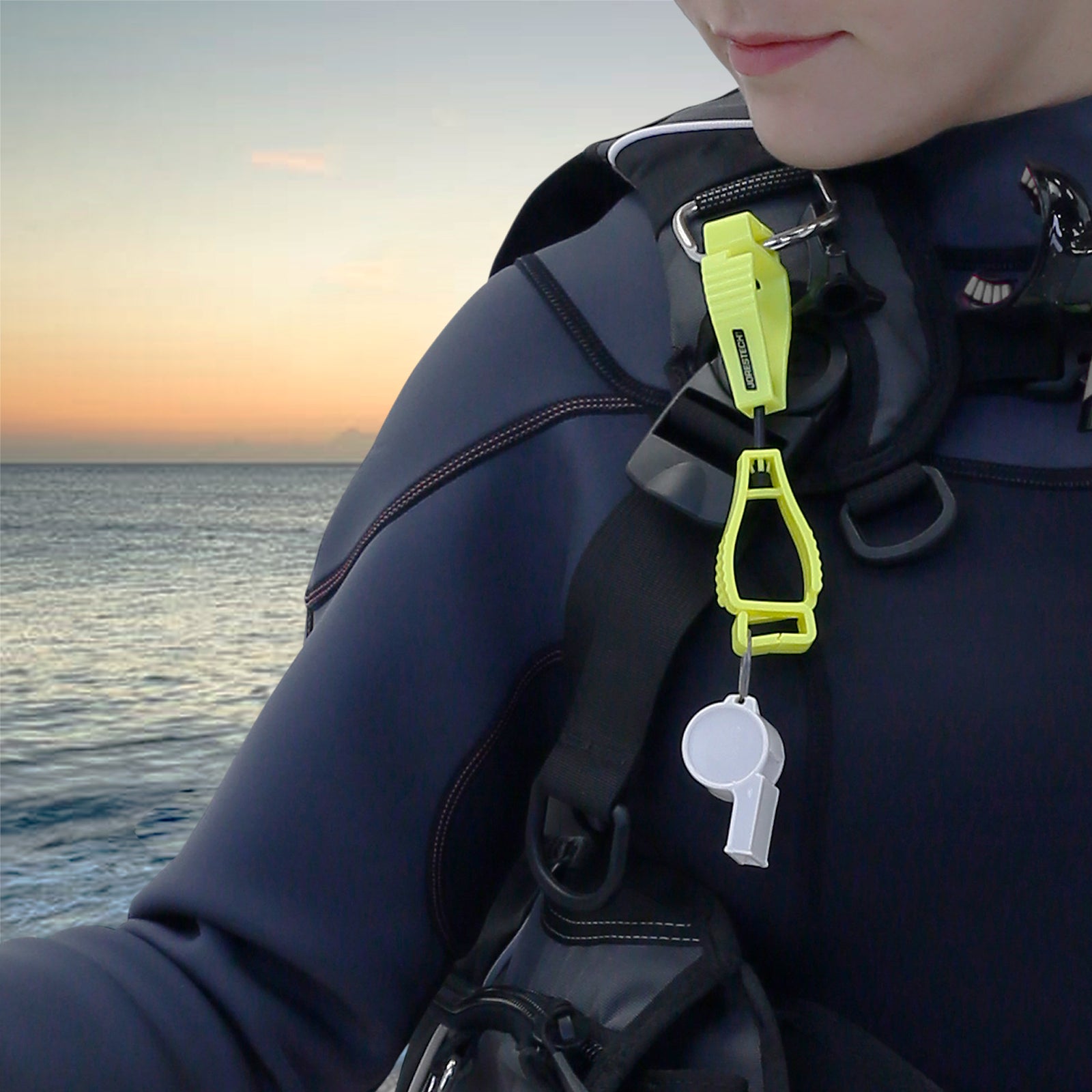 A woman wearing a scuba gear with a yellow glove clip safety holder attached to a D ring on her gear with an emergency whistle hooked on one end. 