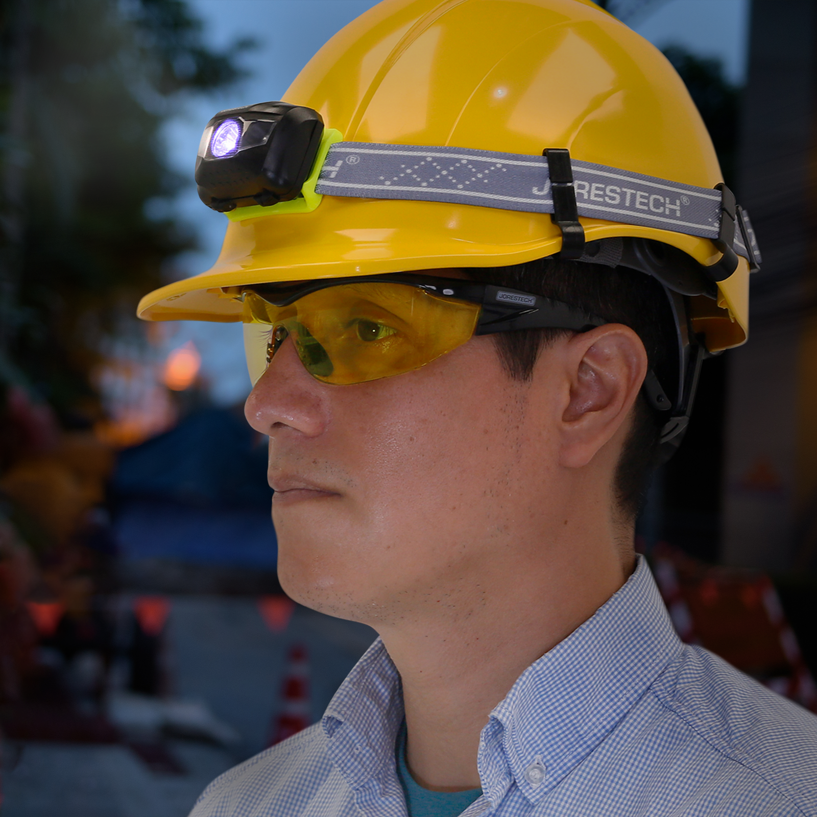 A worker wearing a yellow hard hat with a headlamp attached to it with the Jorestech hard hat headlamp clips. The is a dark blur background with road signs.