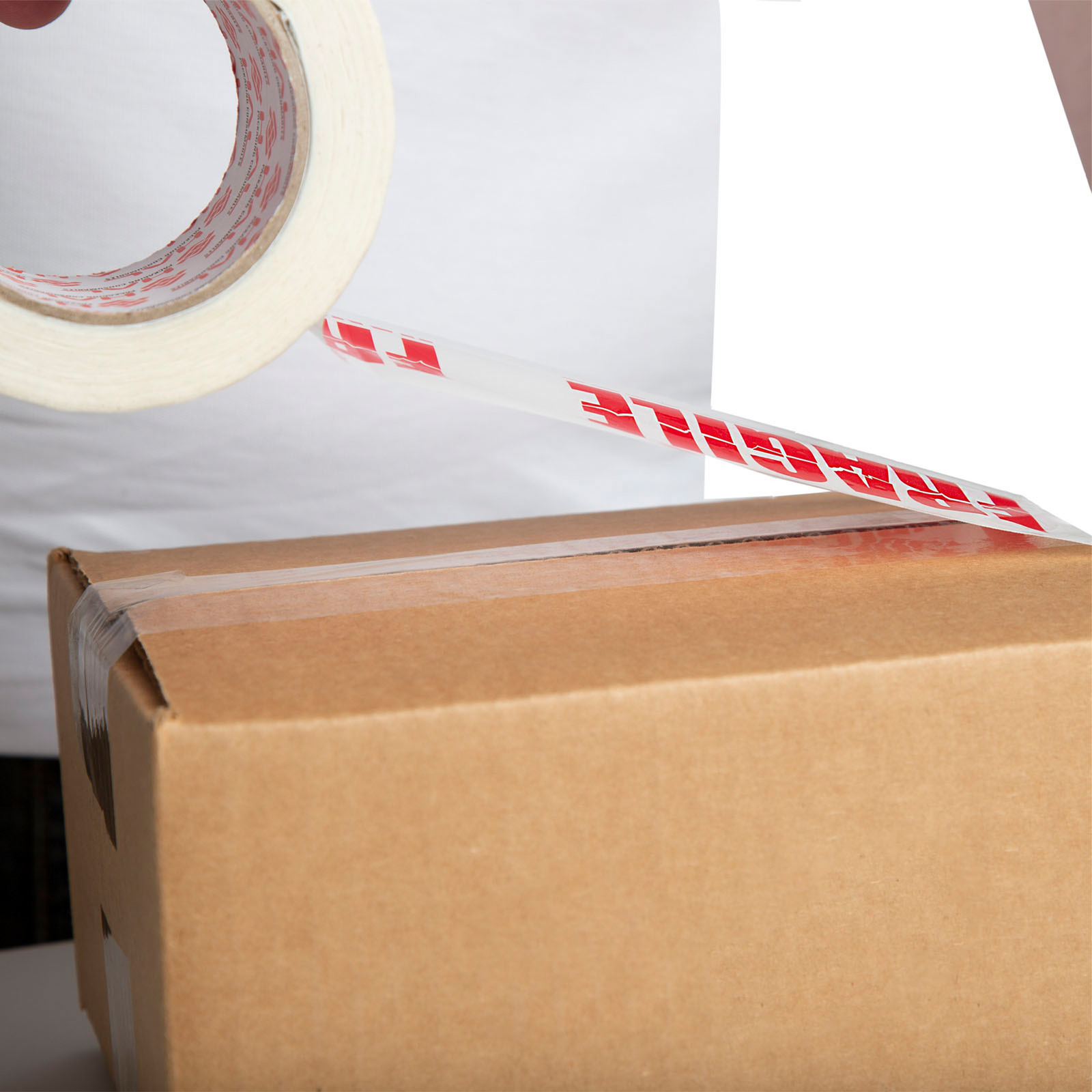 person wearing white shirt using white printed tape fragile to tape together brown box
