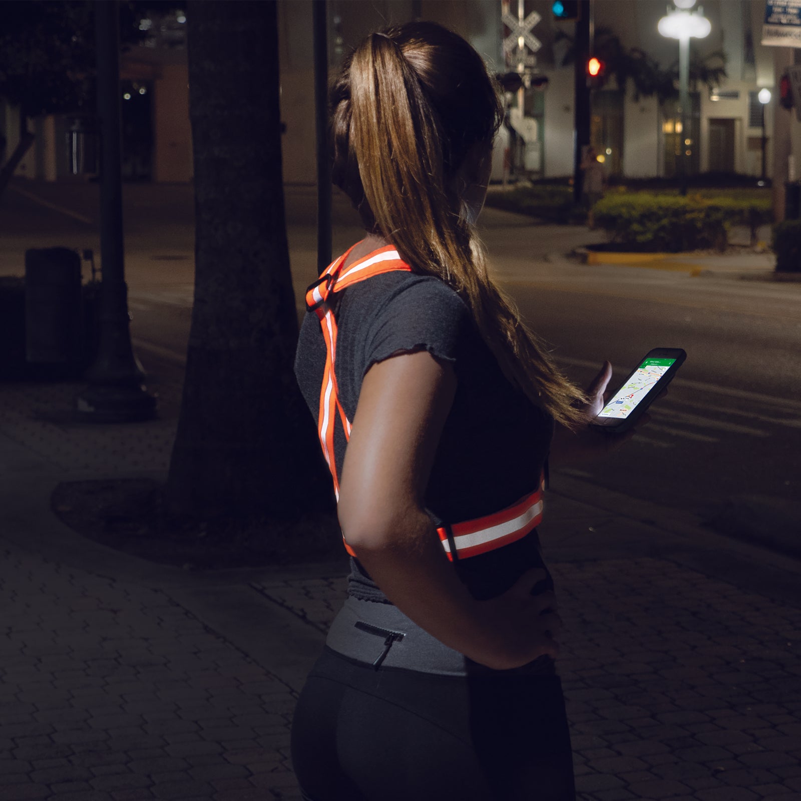 A woman wearing an orange JORESTECH safety suspender doing exercise on the street during night time