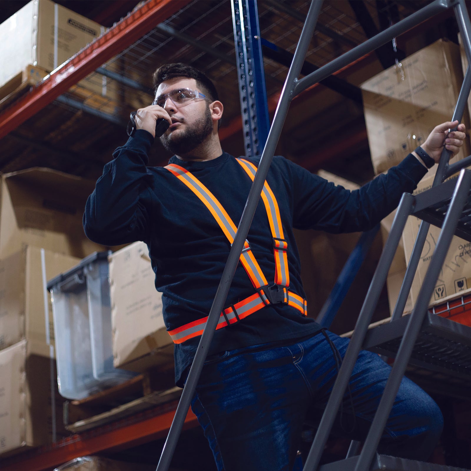 A worker wearing an orange adjustable safety suspender while he is on top of a ladder