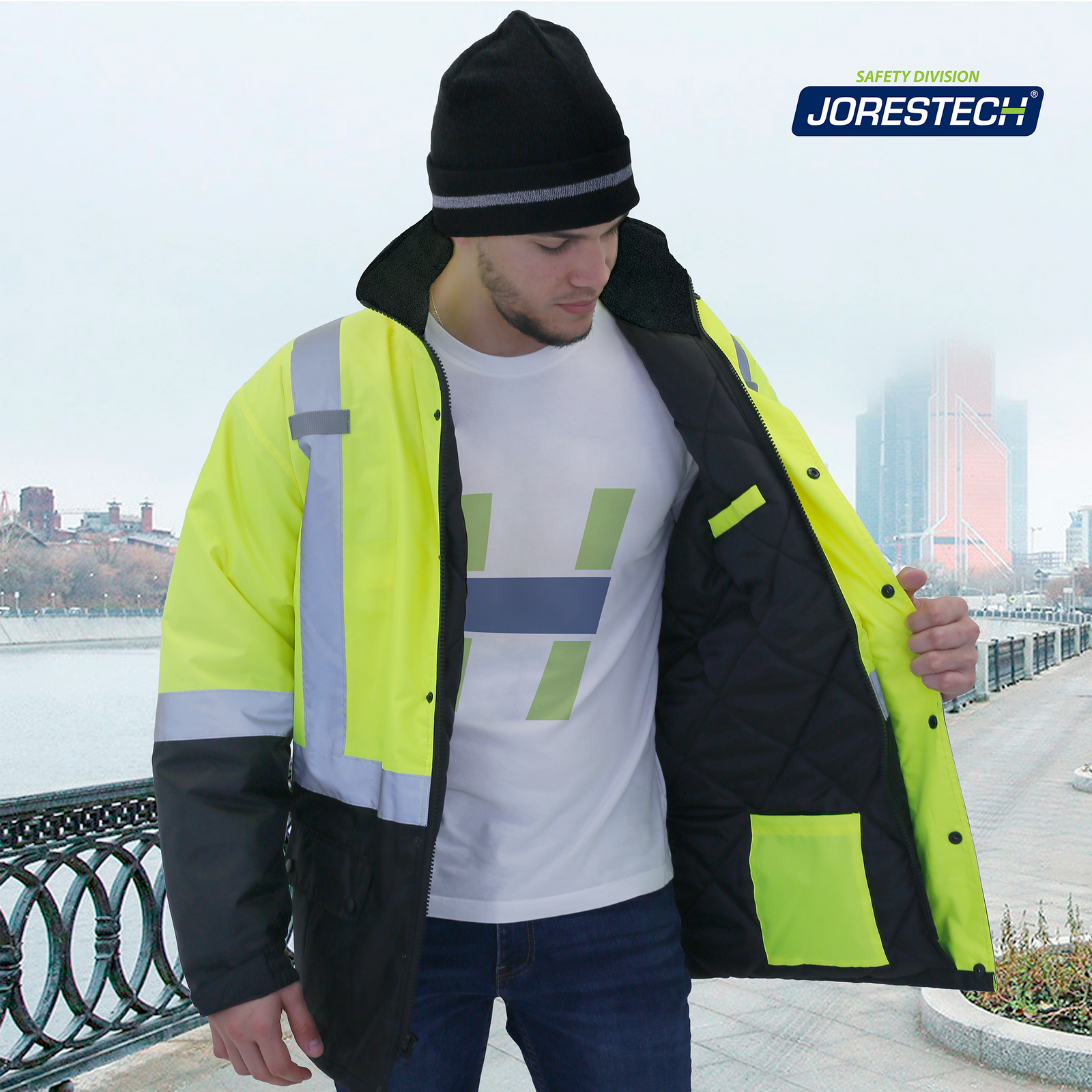 Man in a city wearing the ANSI compliant hi-vis yellow and black JORESTECH parka safety jacket with pockets and reflective stripes. The man is searching for something inside the pockets located in the inner layer of the safety parka jacket