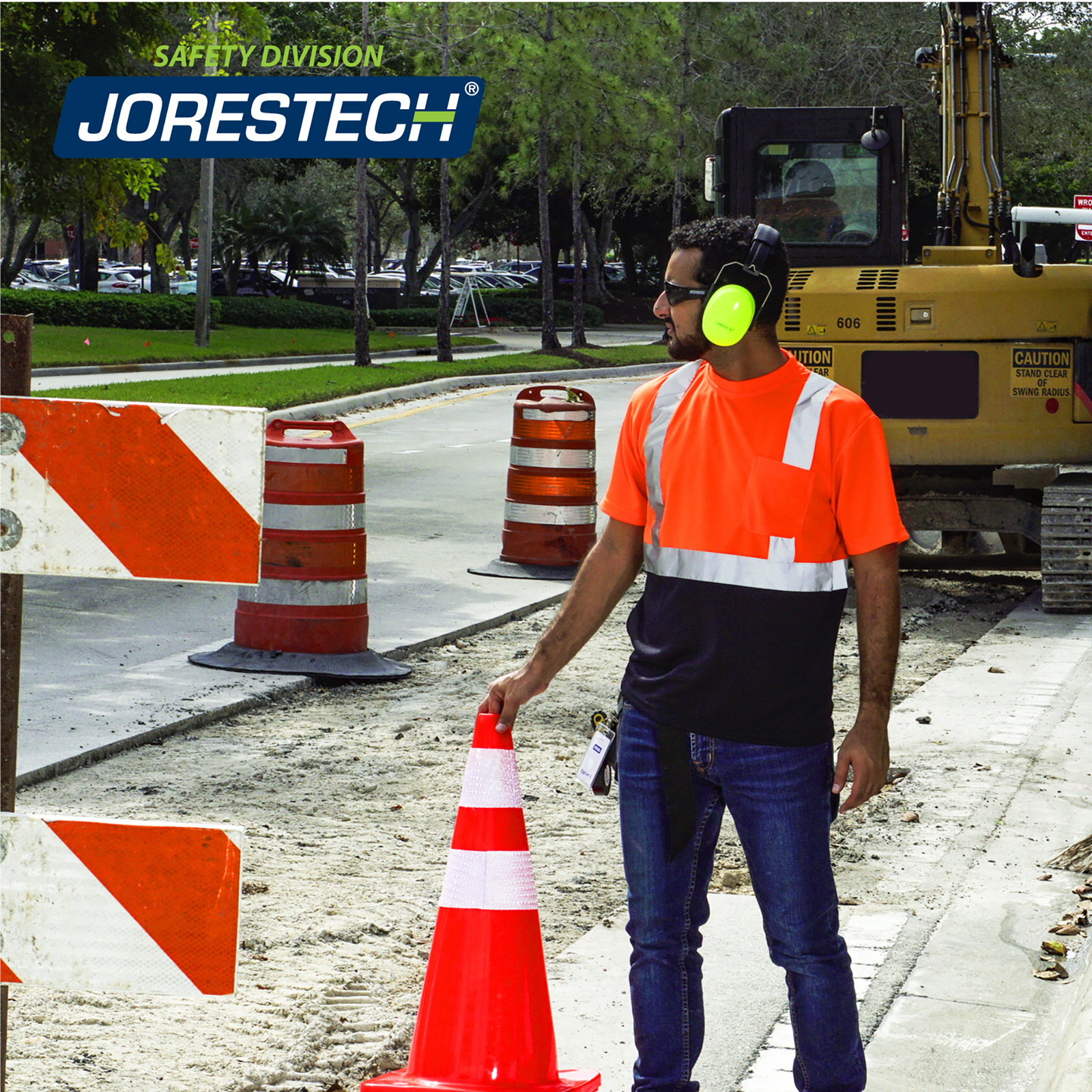 A worker standing in the middle of a road construction while wearing the JORESTECH reflective safety orange shirt. The is a large yellow truck in the background