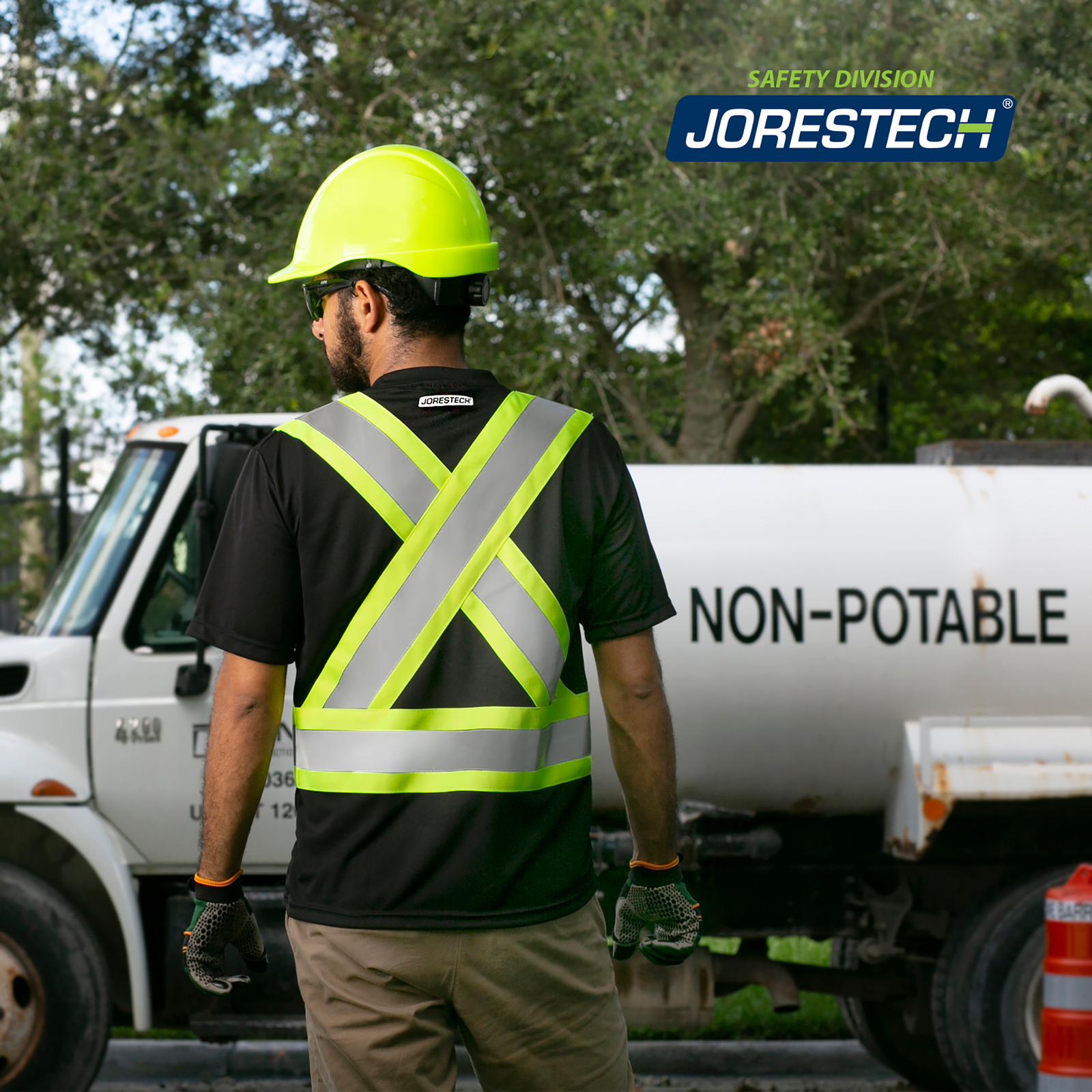A man wearing a black and lime jorestech sort sleeve reflective safety shirt while standing beside a truck 