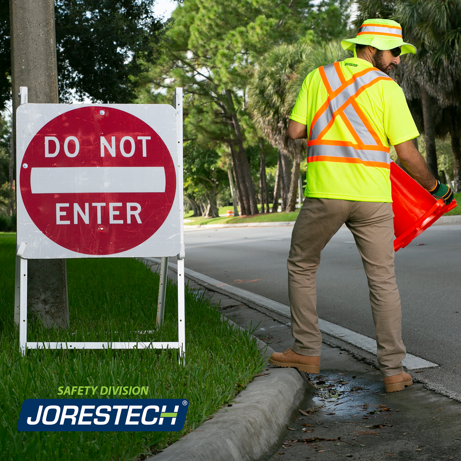 A worker wearing a JORESTECH safety shirt. He is placing signals in the middle of the road to direct the traffic.