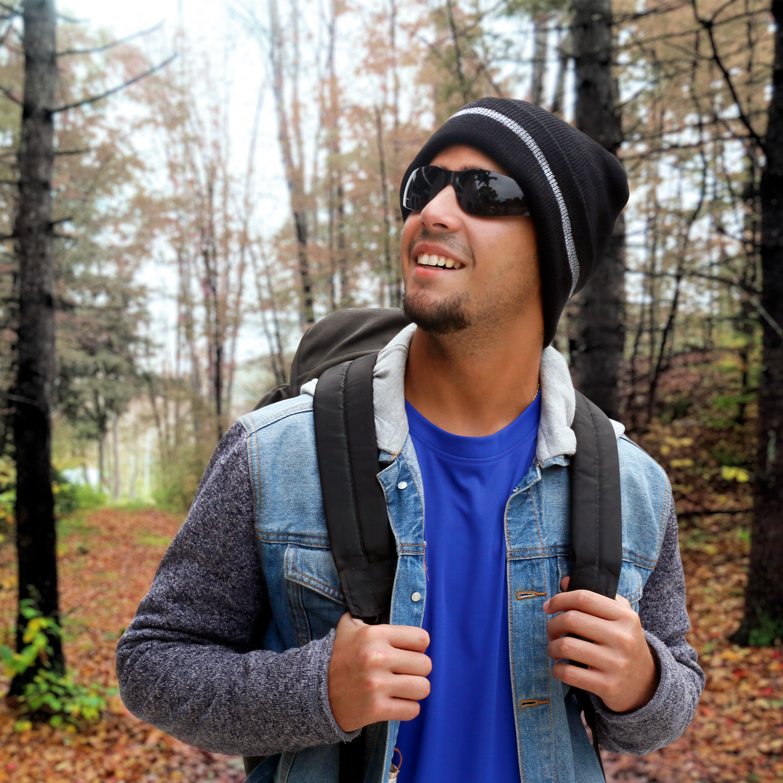 A man wearing the black beanie with reflective stripes while highking in the woods with a back pack and a warm jacket