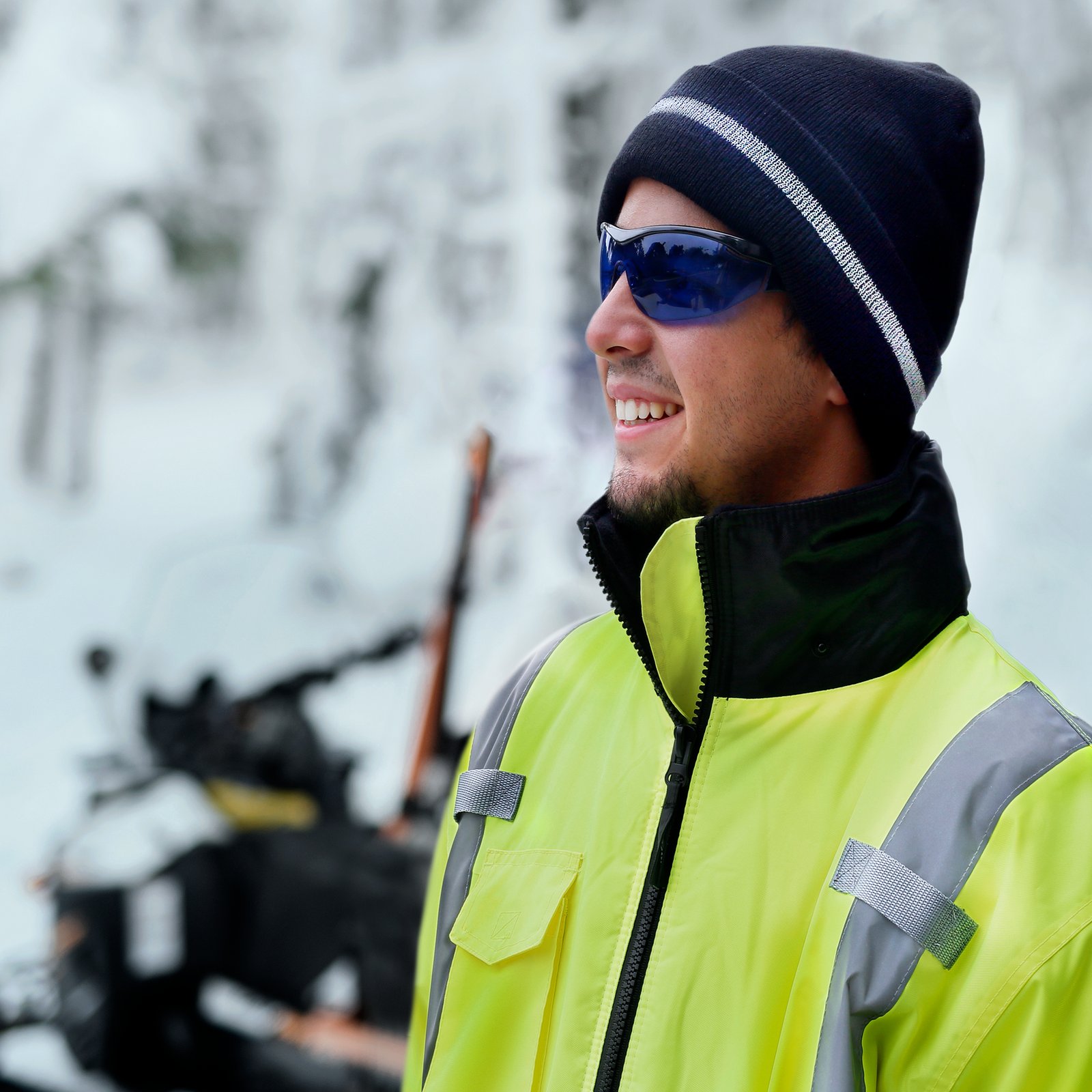 A worker wearing the black JORESTECH® reflective beanie hat and a vi-vis jacket while riding a snow mobile 