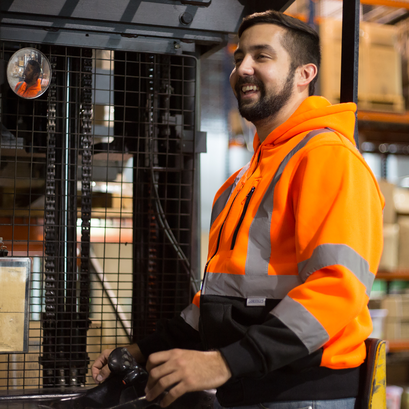 Worker wearing an orange JORESTECH safety sweatshirt with reflective stripes while he is driving a forklift