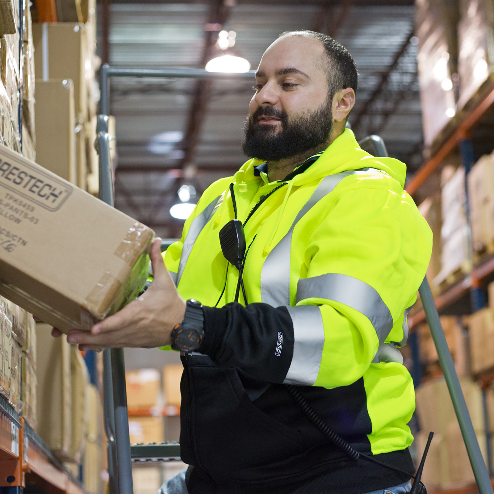A worker wearing a yellow hi-vis safety sweater class 2 tupe R. He is removing a box from a bin a  setting of a warehouse.