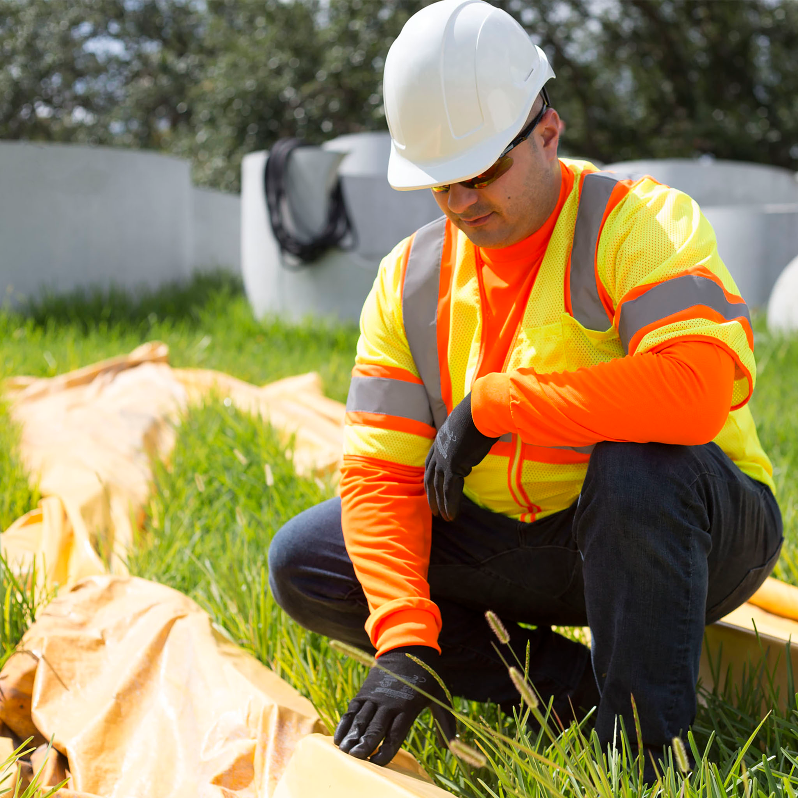 A worker in a construction site. He is wearing an orange long sleeve shirt underneath safety reflective vest
