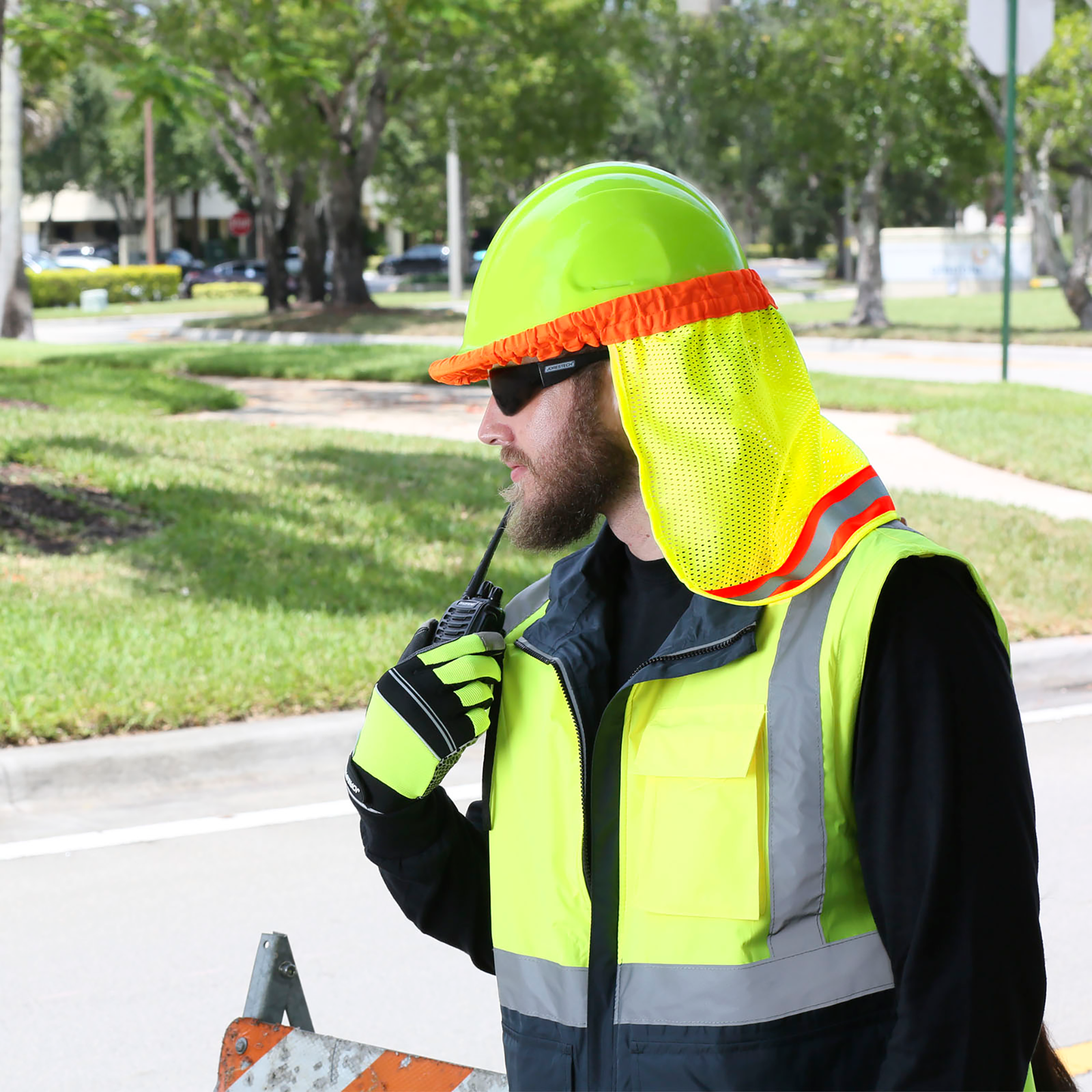 A man wearing a lime cap style hard hat with a JORESTECH lime neck shade while he is in a construction on the road.