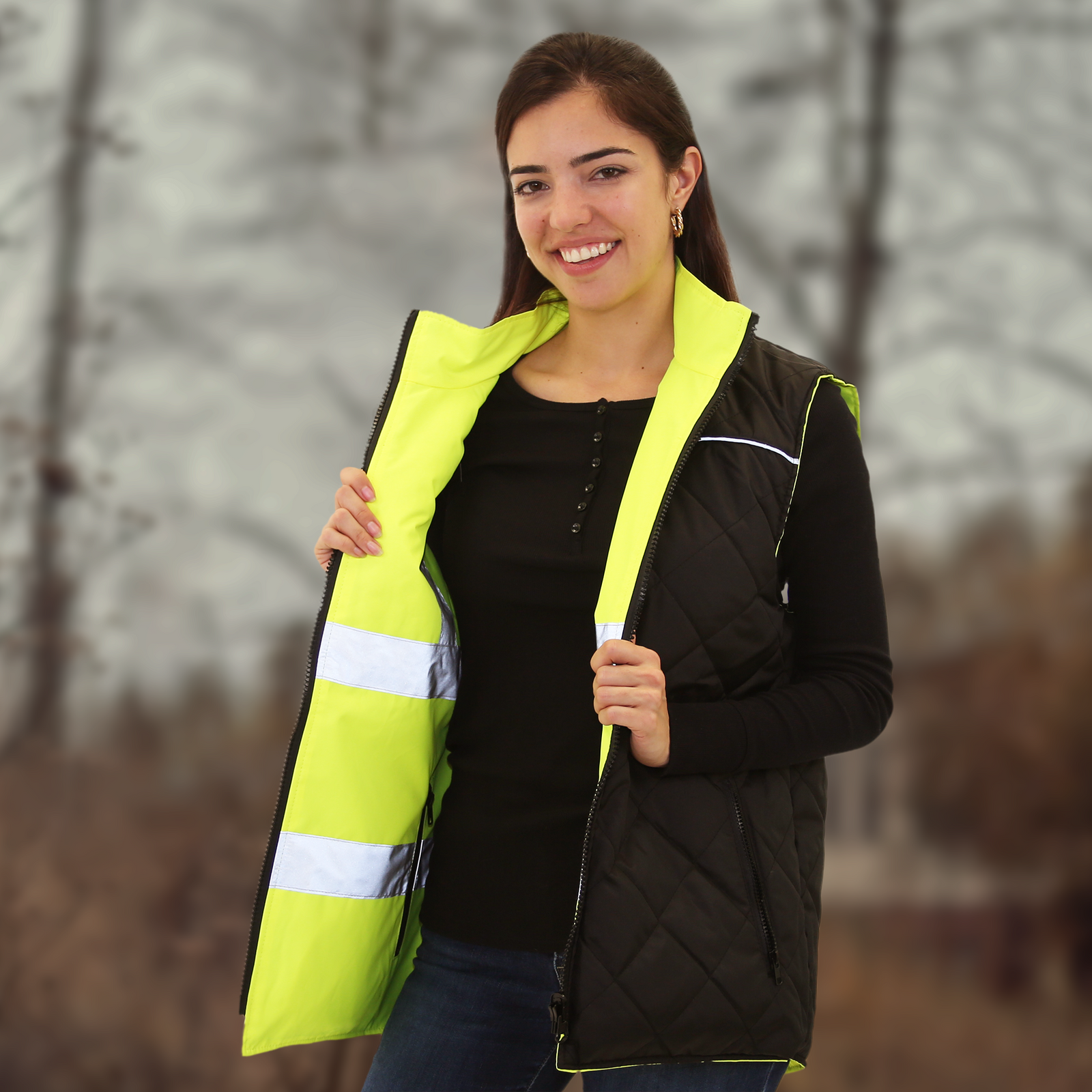 Woman wearing the hi vis JORESTECH yellow black reversible insulated safety vest with reflective strips while surrounded by trees during autumn