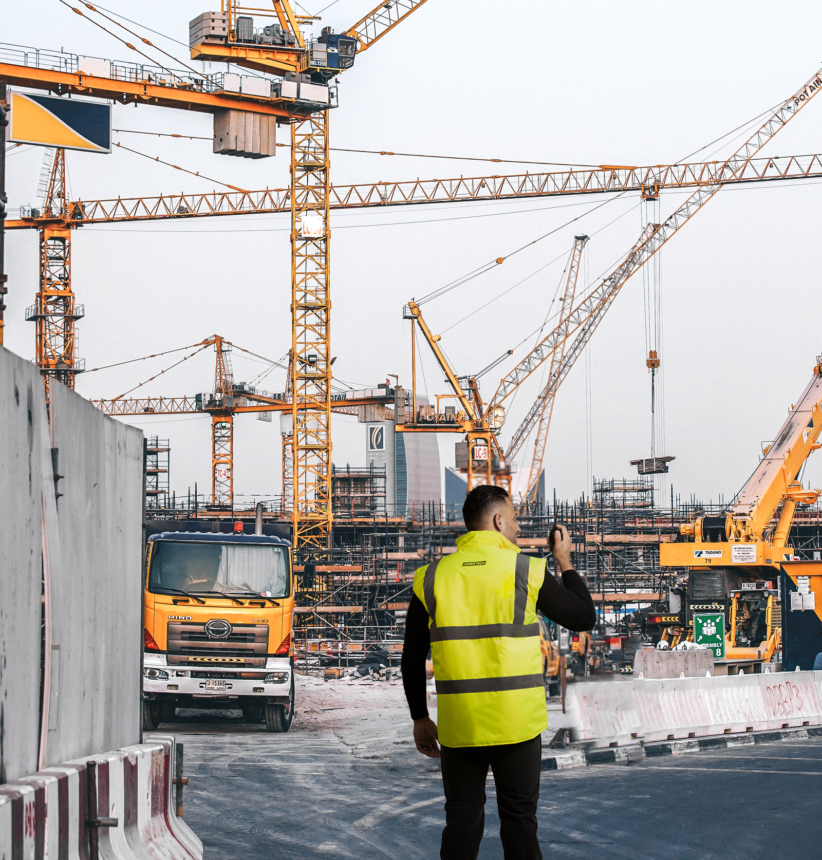 A man wearing the hi visibility yellow black reversible insulated safety vest while he is talking on the radio in a construction site
