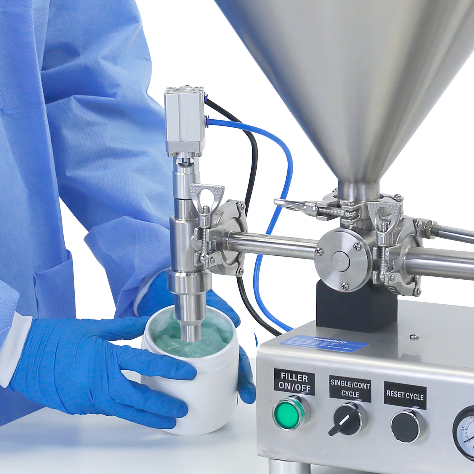 Worker wearing PPE clothing and disposable gloves standing in front of the nozzle of a Piston filler. He is removing a container of 100 ml full of a blue viscos gel after been filled by the stainless steel JORESTECH piston filler that is placed on top of a working table