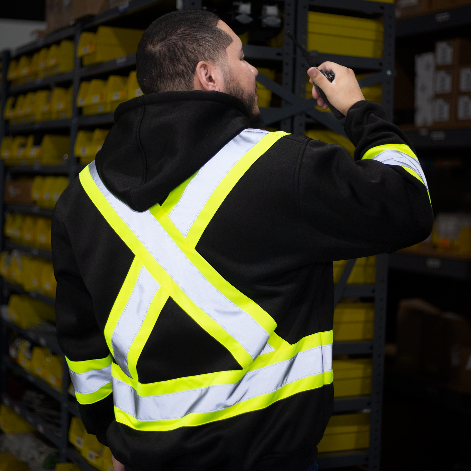 Worker wearing the hi vis safety sweatshirt inside a dark storage room. reflective stripes X on the back of sweater is glowing in the dark.
