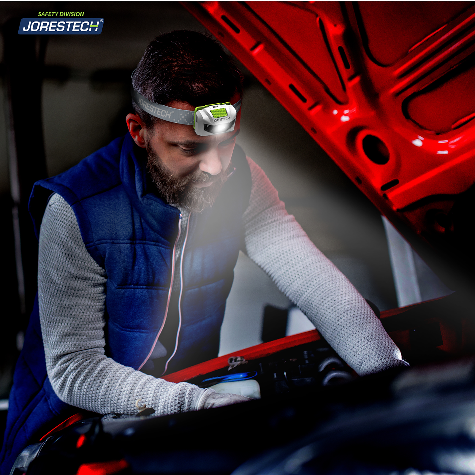 A man wearing a JORESTECH led head lamp while servicing his car at night in the middle of the road.