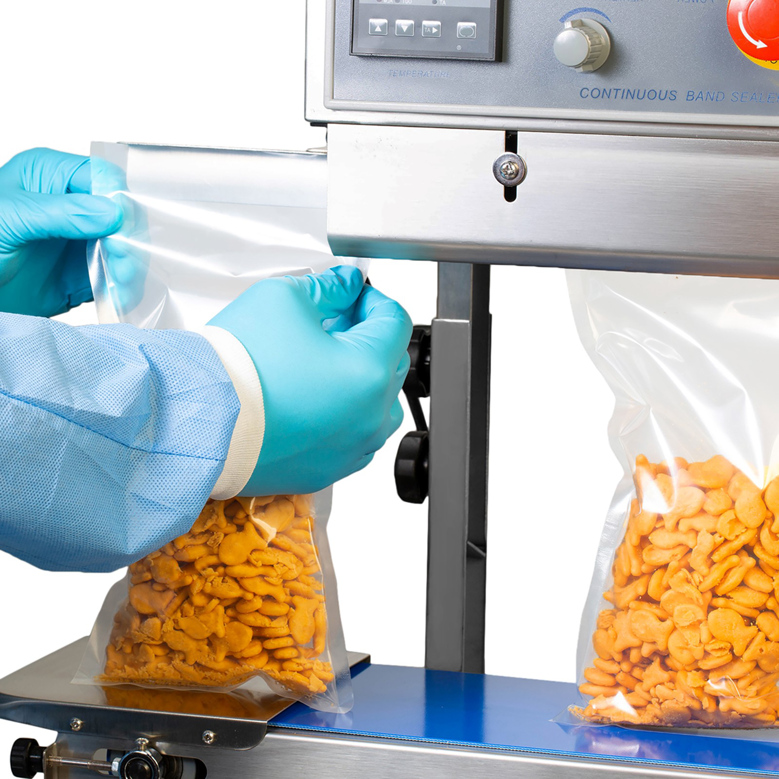 Operator is inserting several plastic bags filled with crackers through the left side of the JORESTECH continuous band sealing machine to get bags sealed. 
