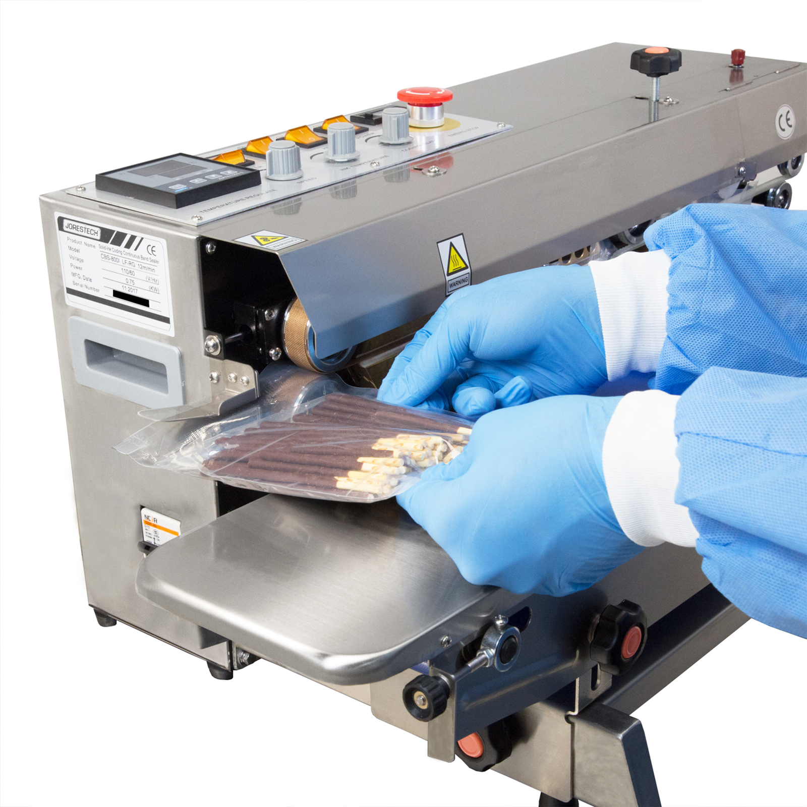 The hands of a person wearing disposable ppe clothing while sealing plastic bags filled chocolate coadded cookies with a Stainless Steel left to right JORES TECHNOLOGIES® continues band sealer set for horizontal applications.