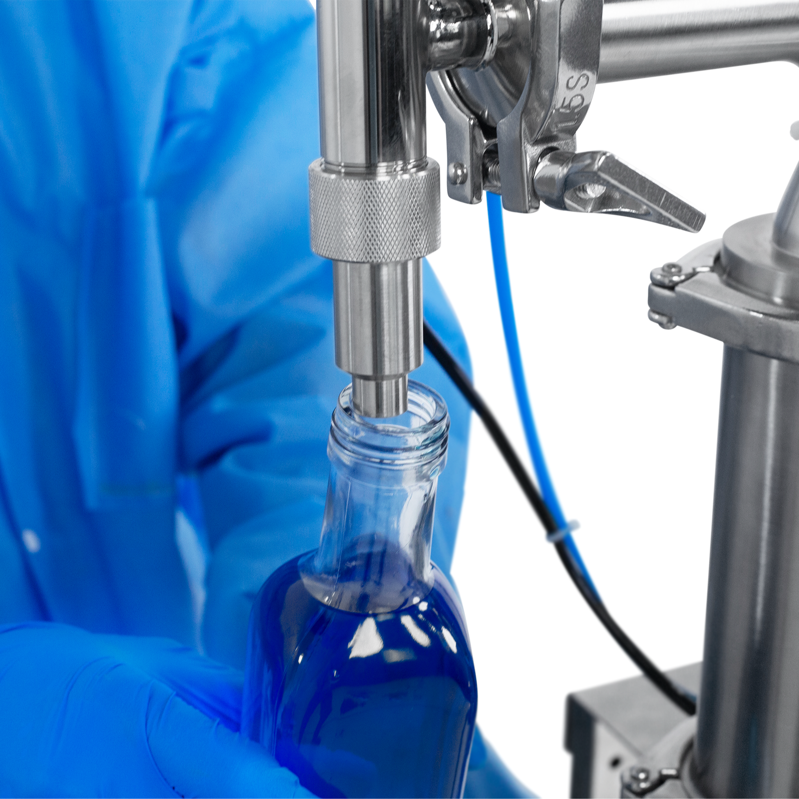 Worker wearing nitrile safety gloves operating the JORES TECHNOLOGIES® Low Viscosity Piston Filler for 1000ml bottles. The person is positioning a 1000ml bottle below the tip of the non-drip nozzle to be filled with accuracy by the liquid filling machine.