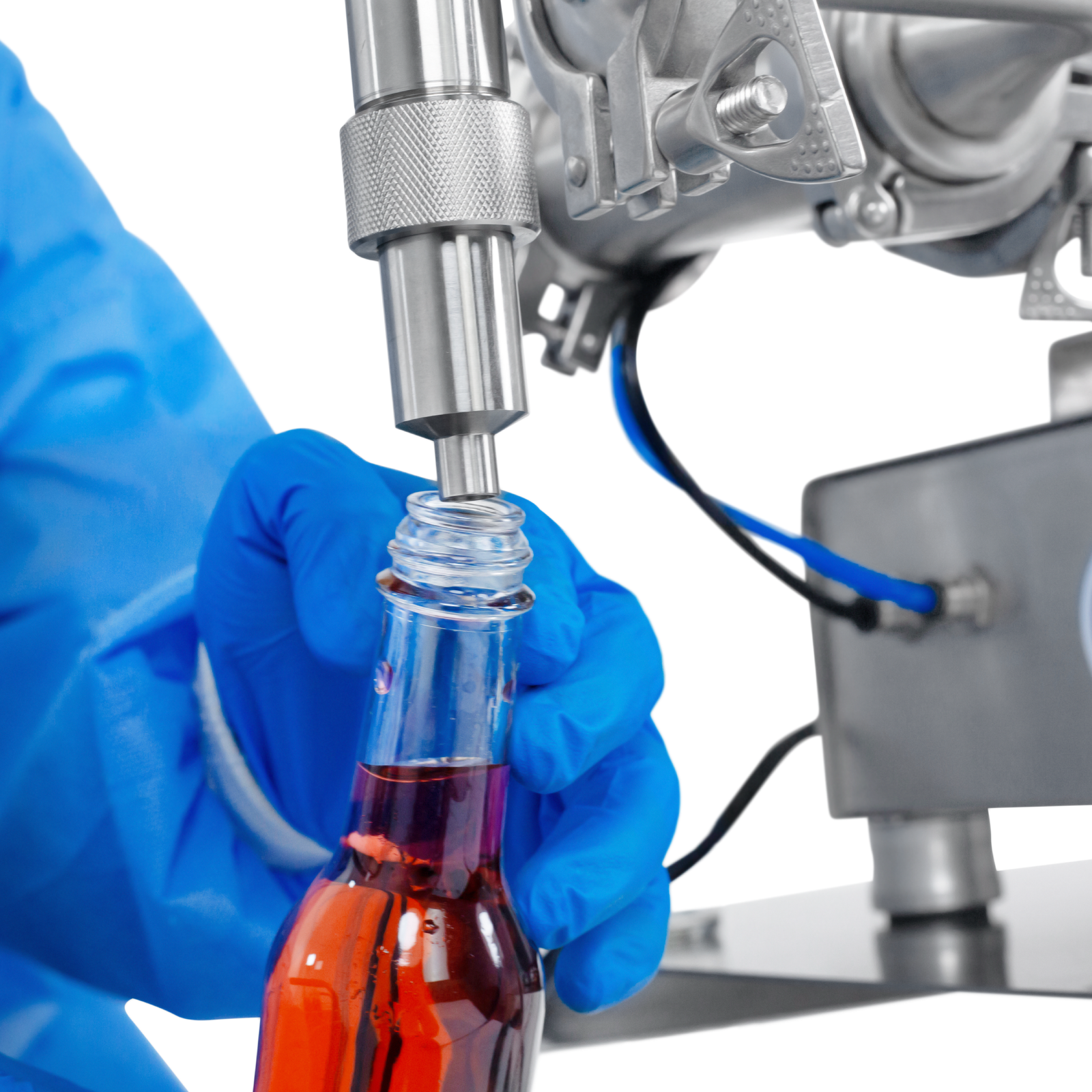 Worker wearing nitrile safety gloves operating the JORES TECHNOLOGIES® Low Viscosity Piston Filler. The person is positioning a 250ml bottle below the tip of the non-drip nozzle to be filled with accuracy by the liquid filling machine.