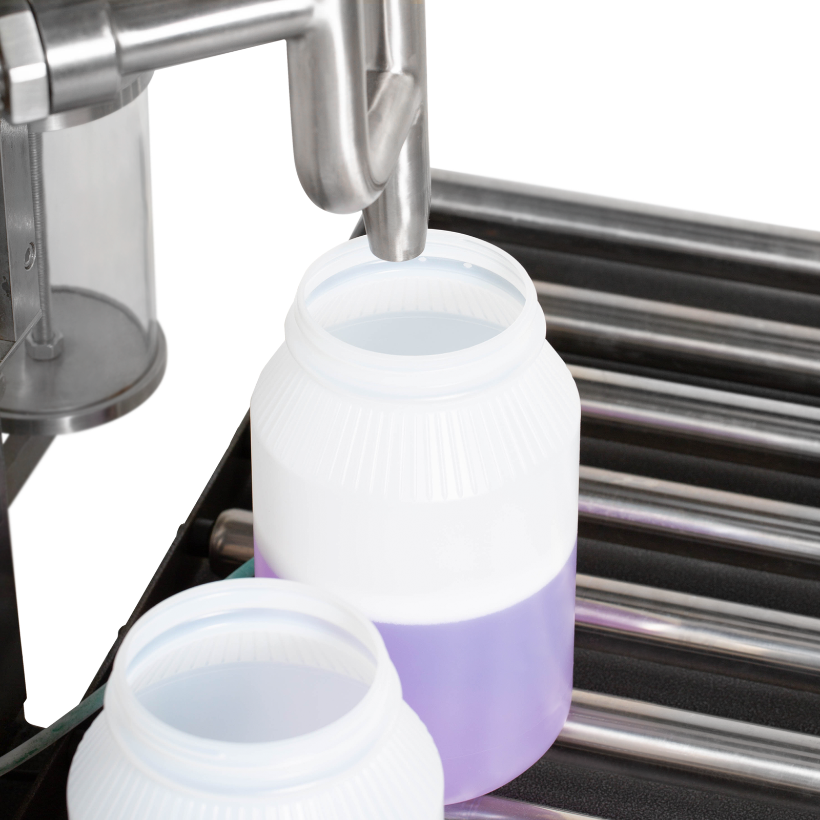 Closeup image shows two extra large containers positioned on top of the roller conveyors. One of them is being filled with a purple solution by the net weight liquid filler