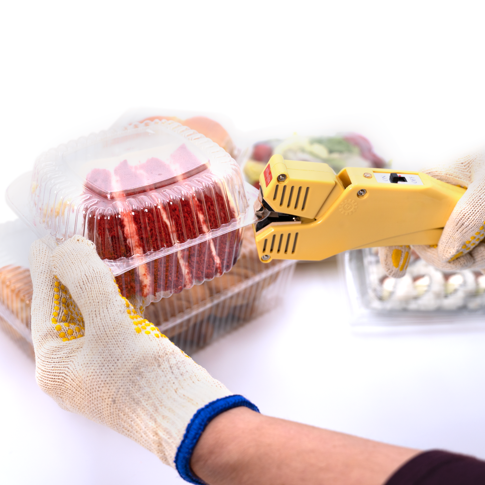 Worker using a manual direct heat clamshell sealer to close several clear boxes filled with vegetable, cookies, sushi, cake etc.