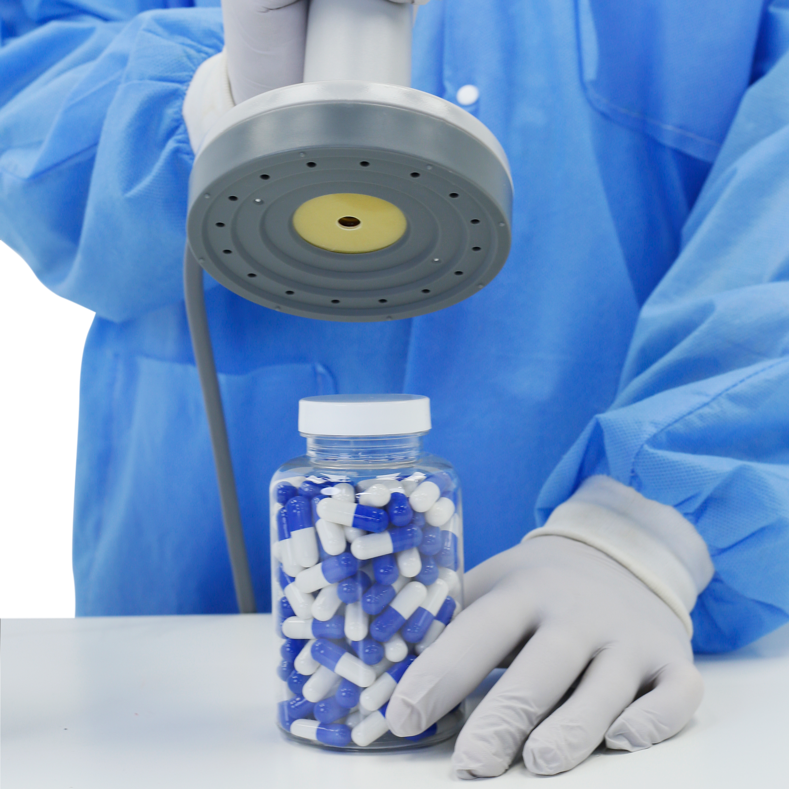 Person in a lab wearing personal protection equipment sealing a bottle of pills using the jorestech induction cap sealer