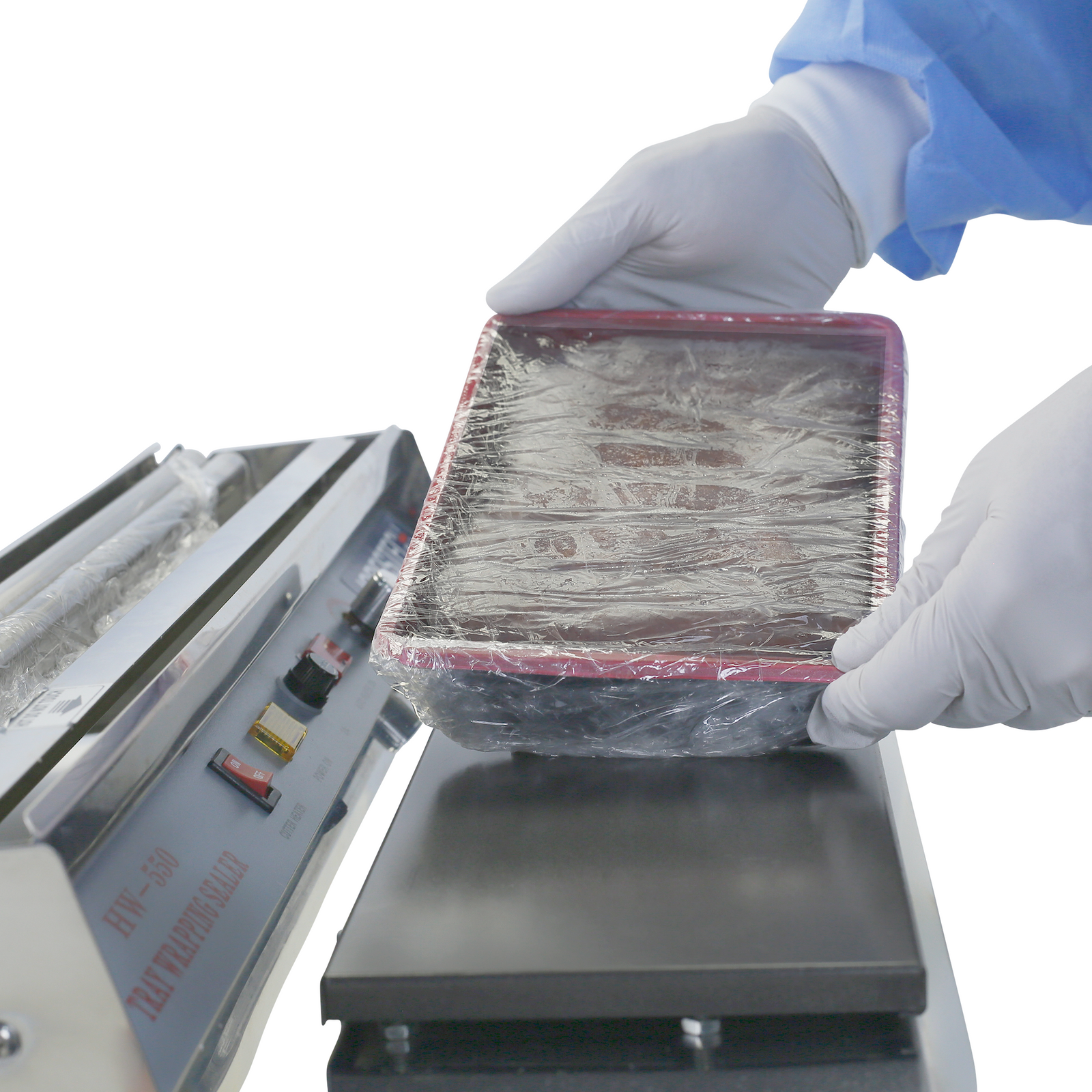 operator wearing white gloves shrink wrapping food tray using manual tray wrapper