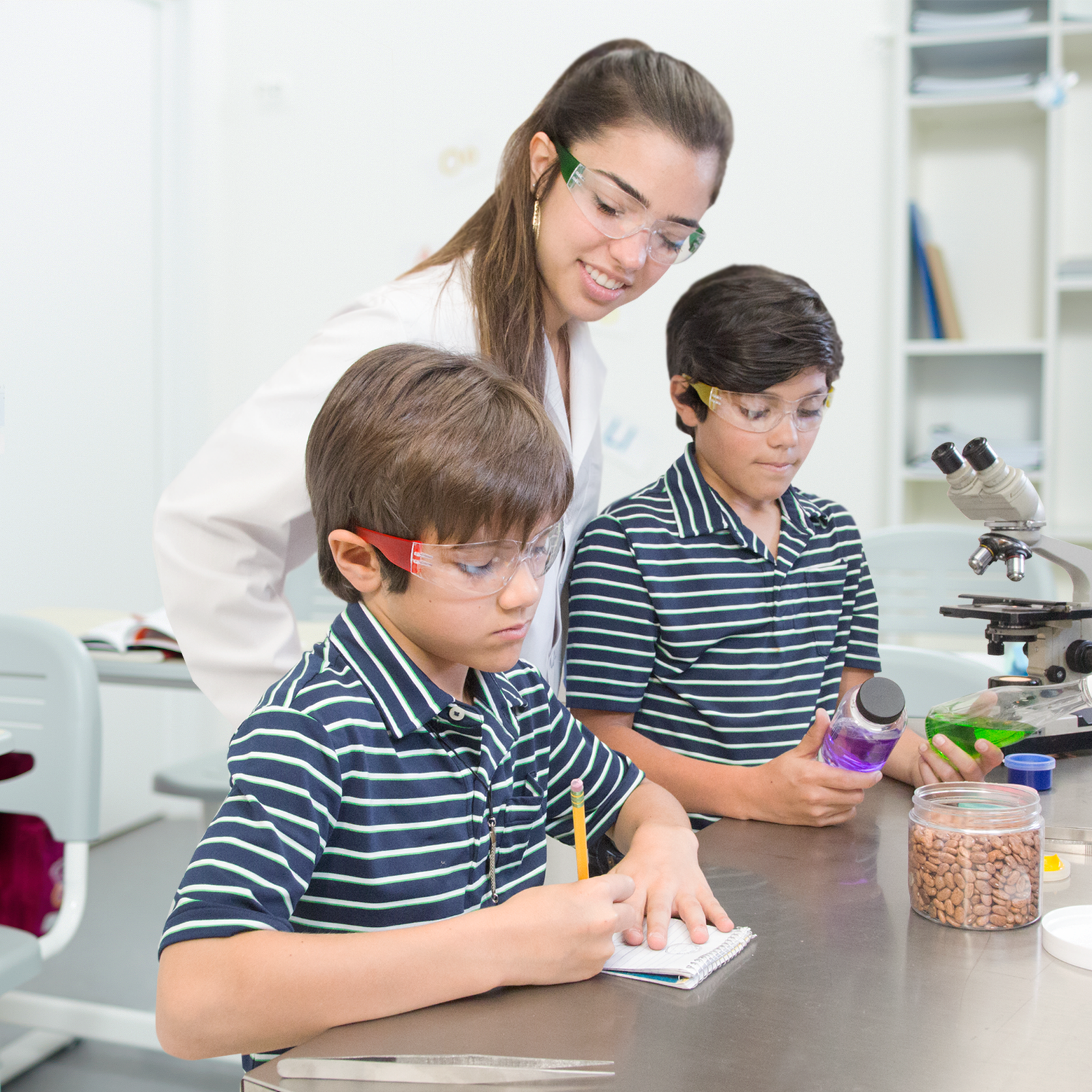 2 boys in uniform and their teacher in a school lab setting wearing JORESTECH multicolor high impact safety glasses
