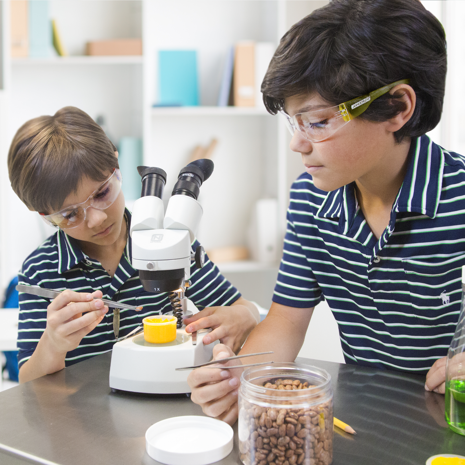 Two boys are wearing JORESTECH safety glasses while they are operating a microscope in la school lab