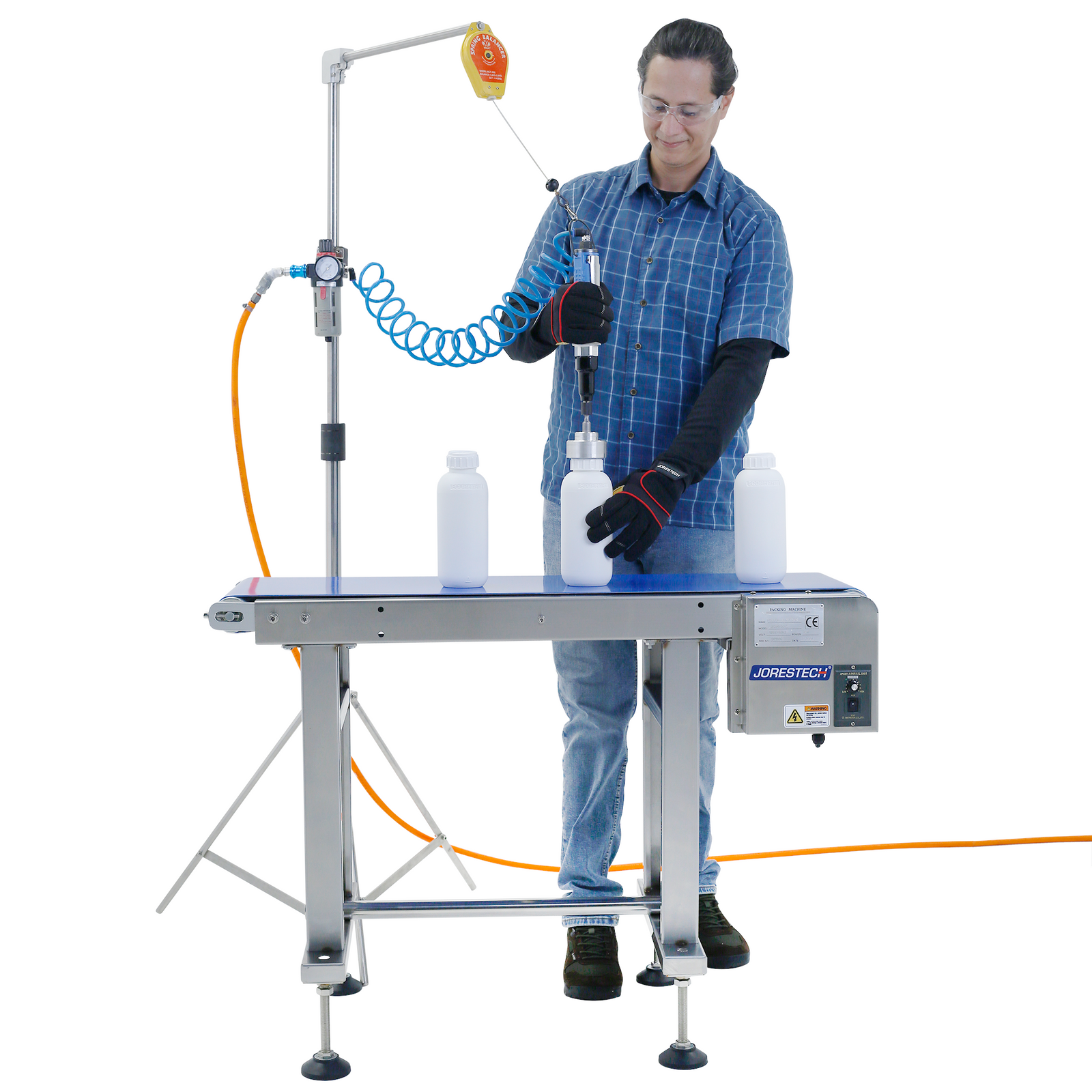 man wearing blue striped shirt and jeans capping white bottles using manual bottle capper hanging on stainless steel tripod