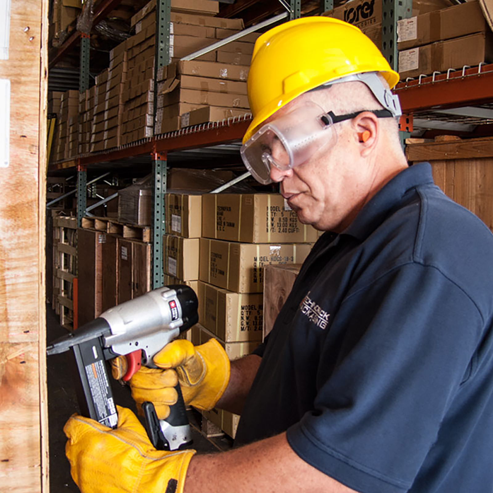 A worker wearing JORESTECH Safety Goggles for Impact Protection while drilling a crate in a warehouse setting