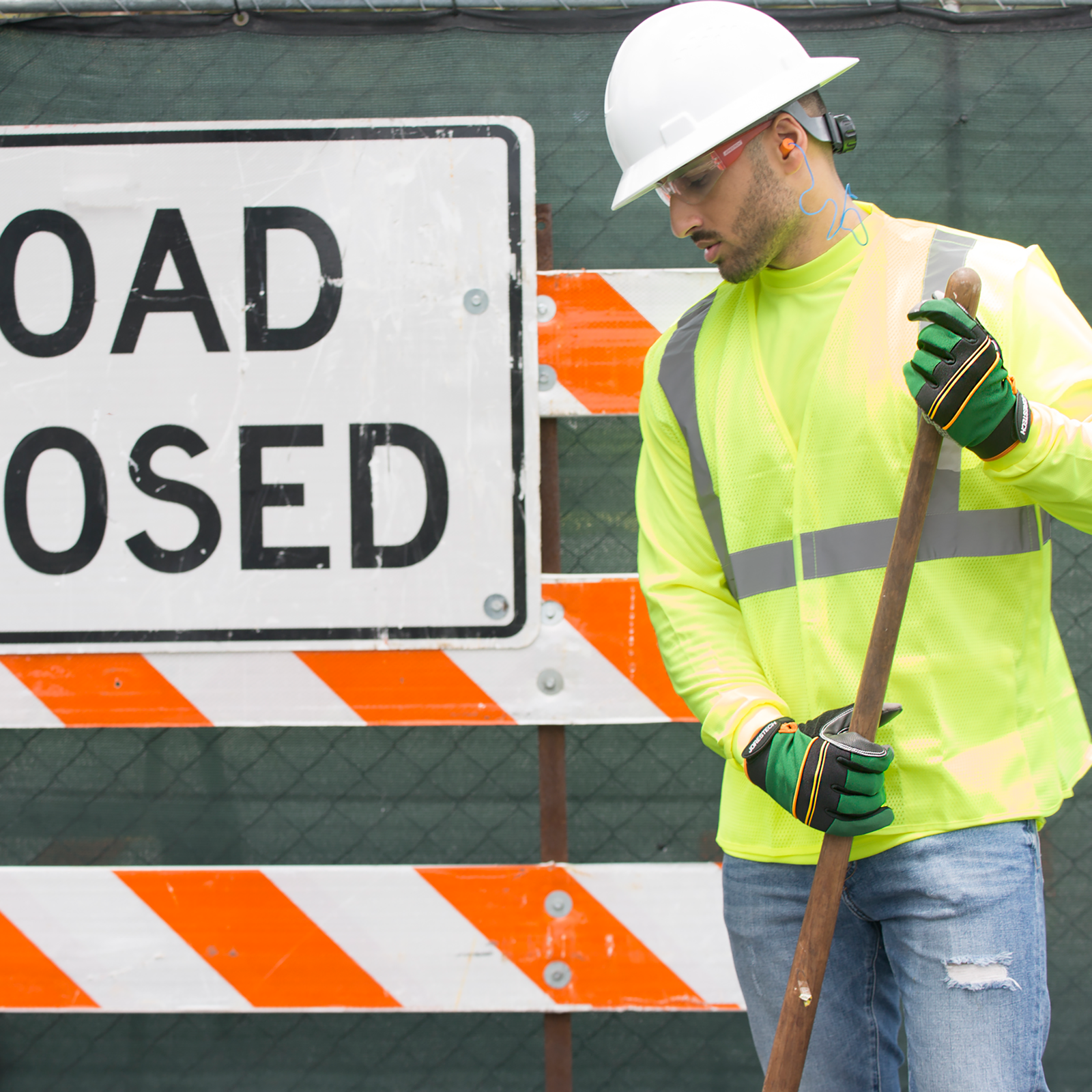 A road worker wearing a white hard hat, safety glasses and the safety work JORESTECH gloves with anti slip silicone dotted palms while doing road construction